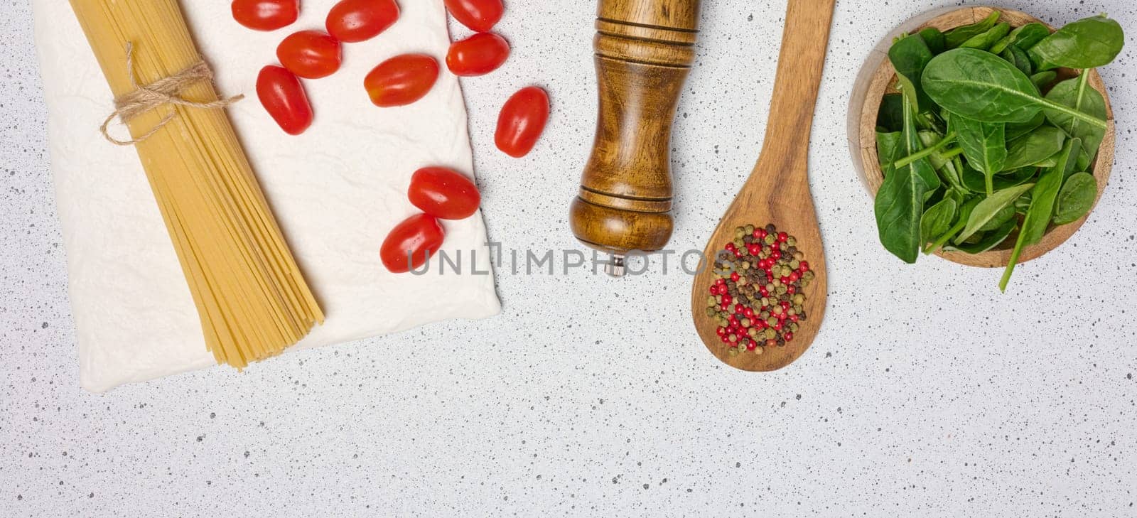 Wooden bowl with spinach, cherry tomatoes on a wooden plate, spoon with spices, uncooked spaghetti tied with twine