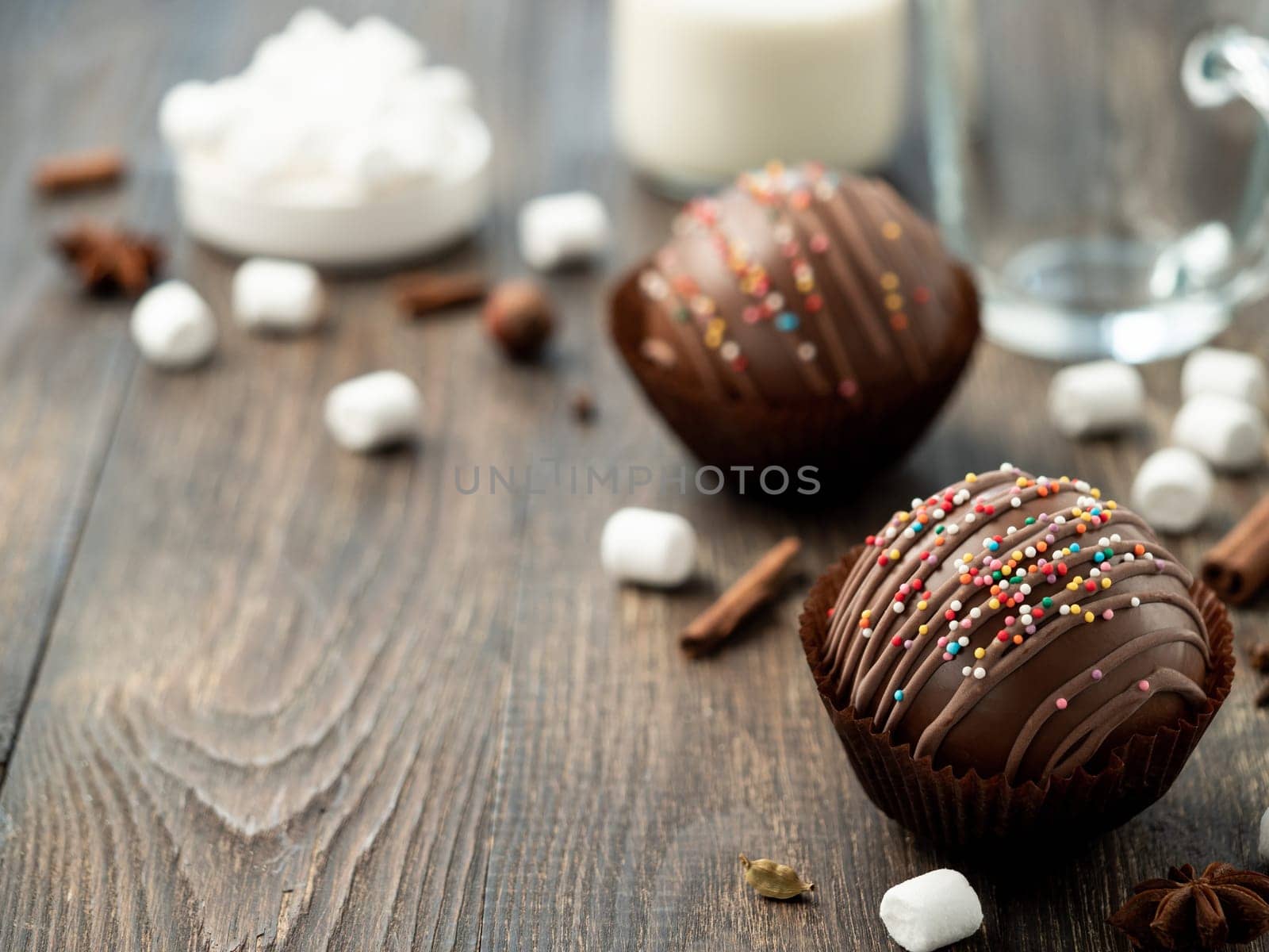 Chocolate cocoa bomb on wooden table near cup and plant-based milk. Ball made from milk chocolate with marshmallow, copy space for text. Trendy winter drink, gift present idea for christmas holidays