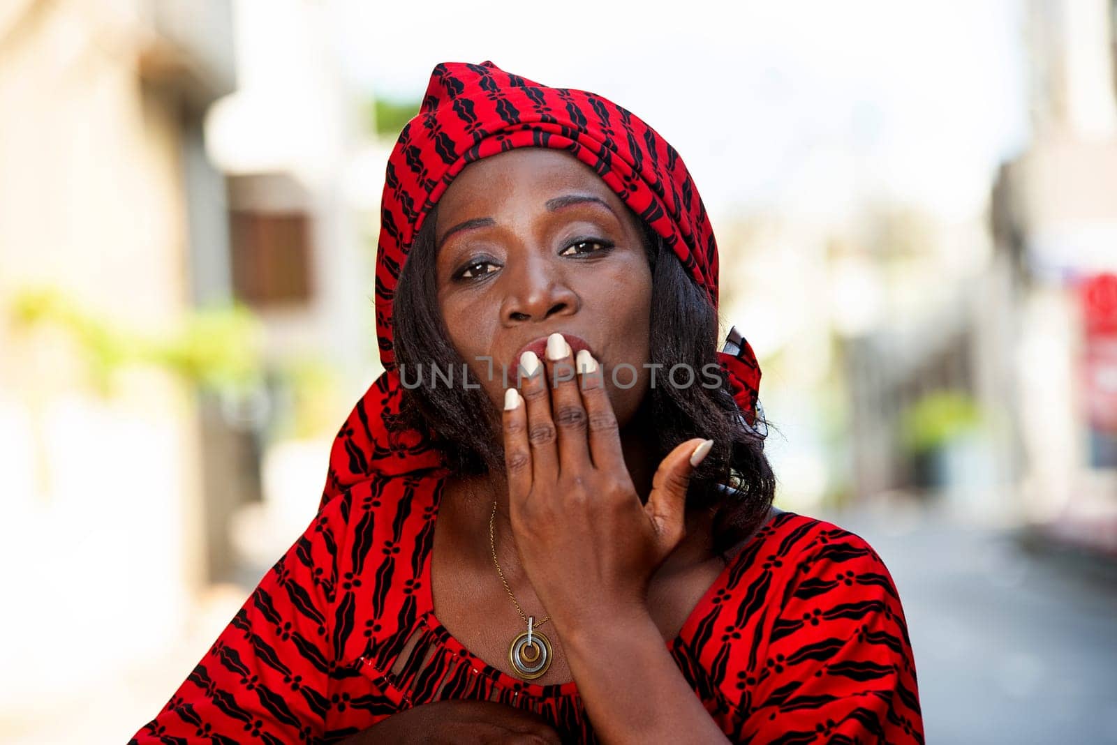 Smiling beautiful young woman in red african outfit makes a flirt on camera. Shopping with love concept