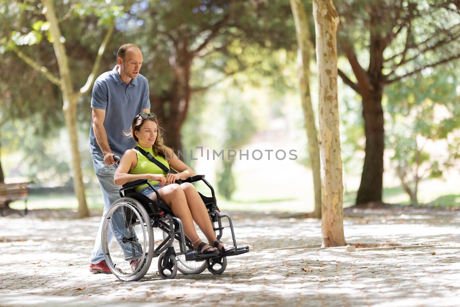 Nurse assisting a smiling young disabled woman in a wheelchair enjoying a sunny day at the park