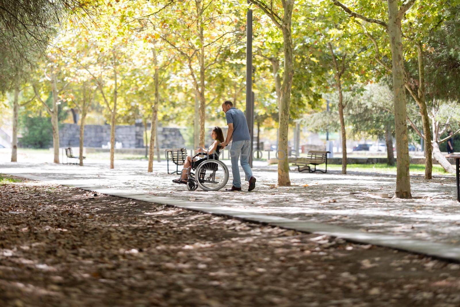 Nurse assisting a female patient in a wheelchair through a sunny park, providing mobility support and enjoying the outdoors