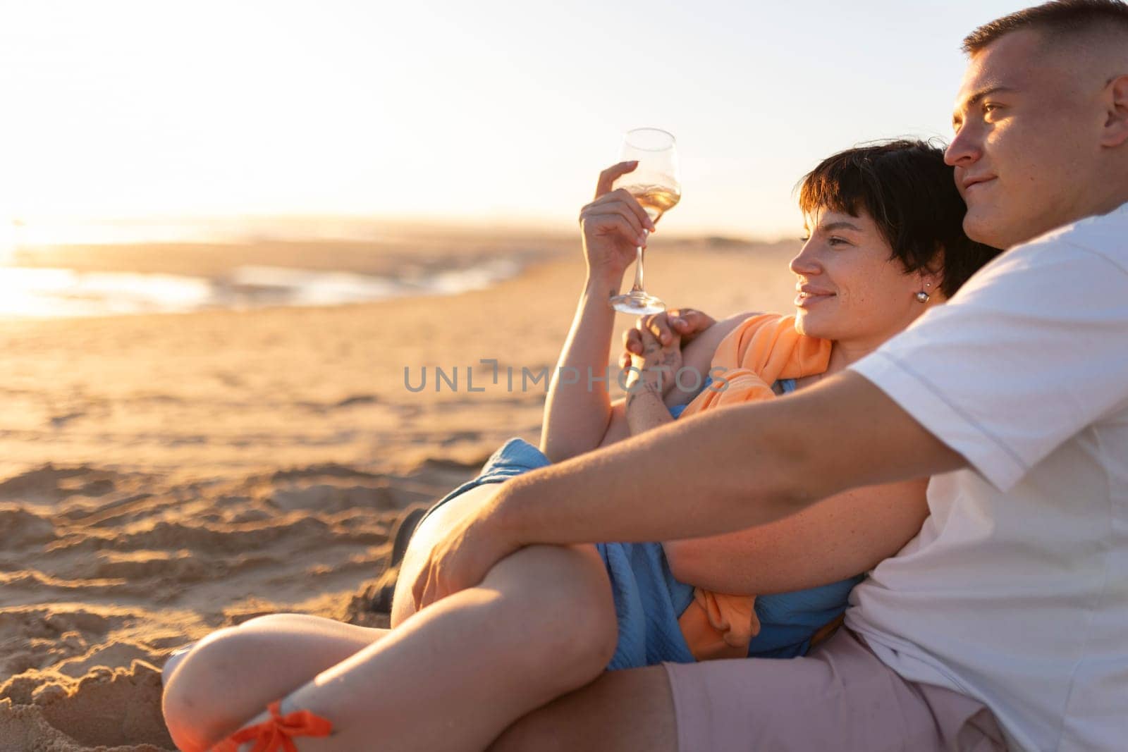 Couple relaxing on the beach at sunset, enjoying a glass of wine and each other's company