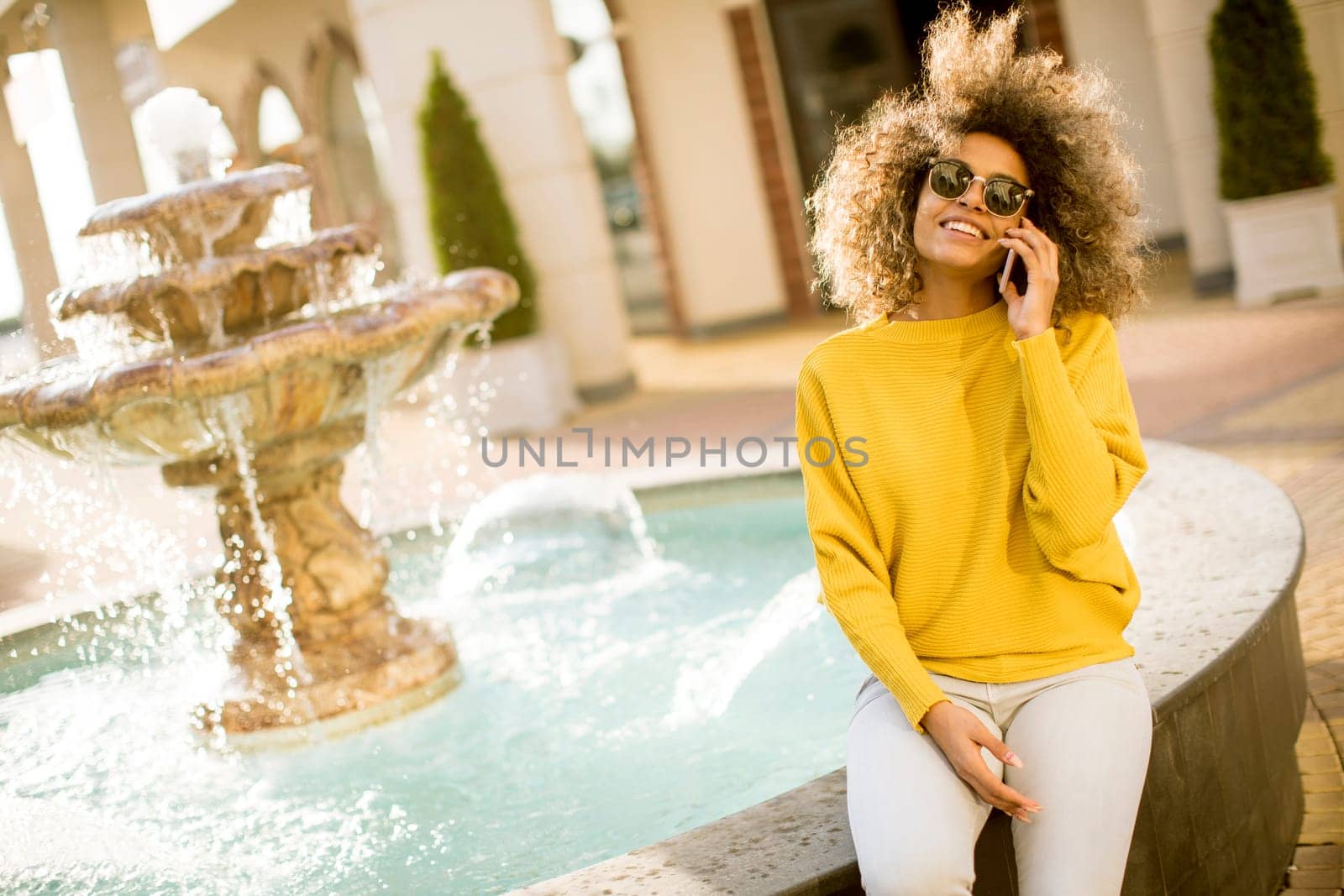 Aftican american young woman sits near fountain and talks on smartphone