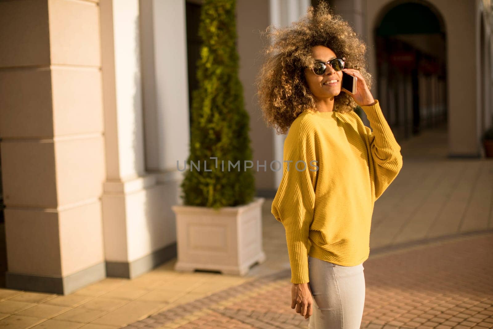 Attractive young woman with curly hair using her touch screen mobile cell phone on the street