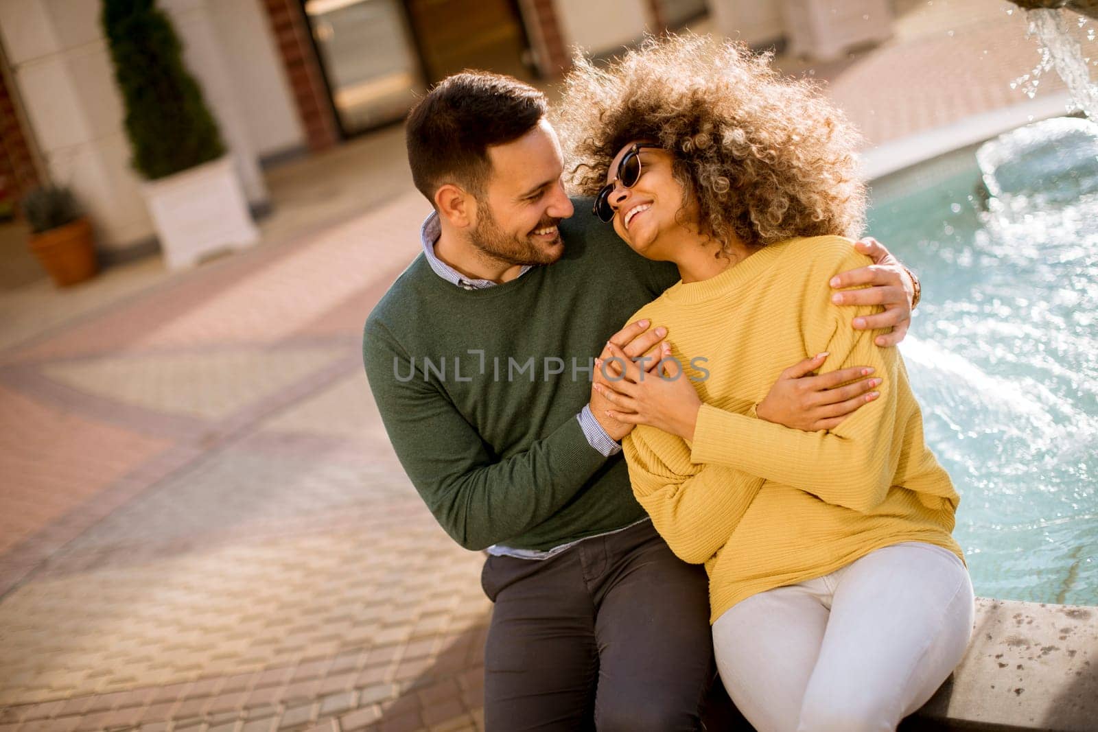 Portrait of beautiful smiling love couple sitting near fountain on a sunny day