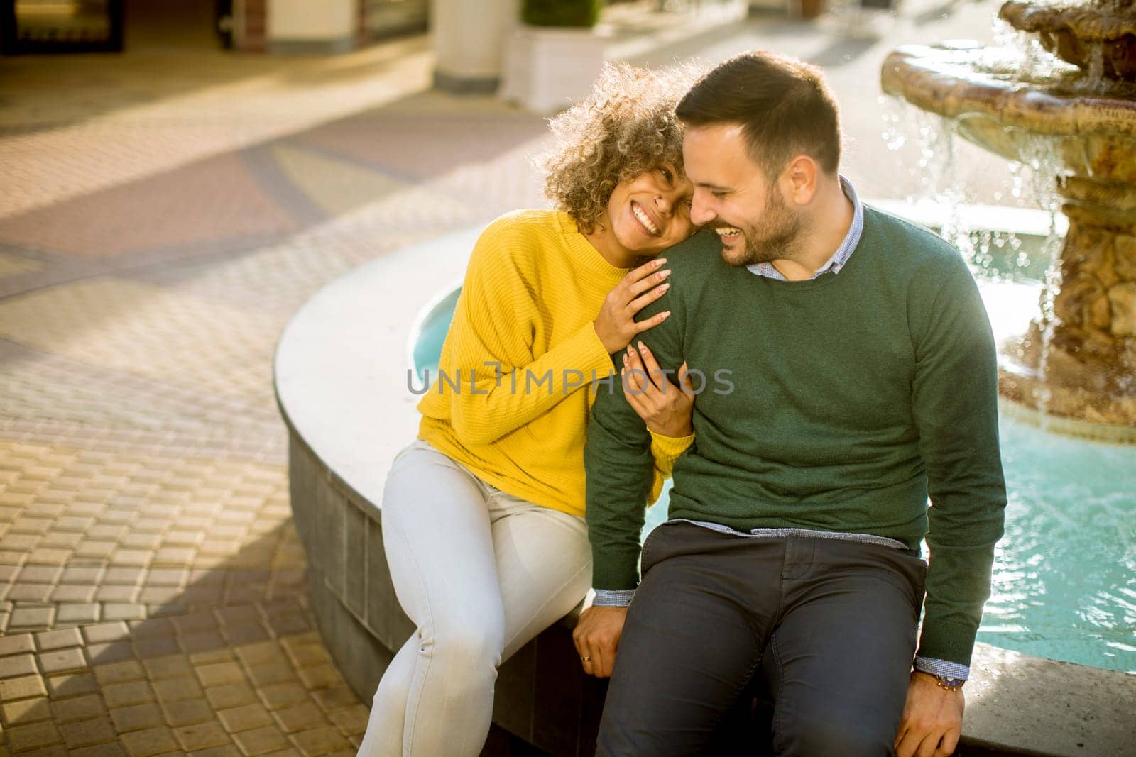 Portrait of beautiful smiling love couple sitting near fountain outdoors
