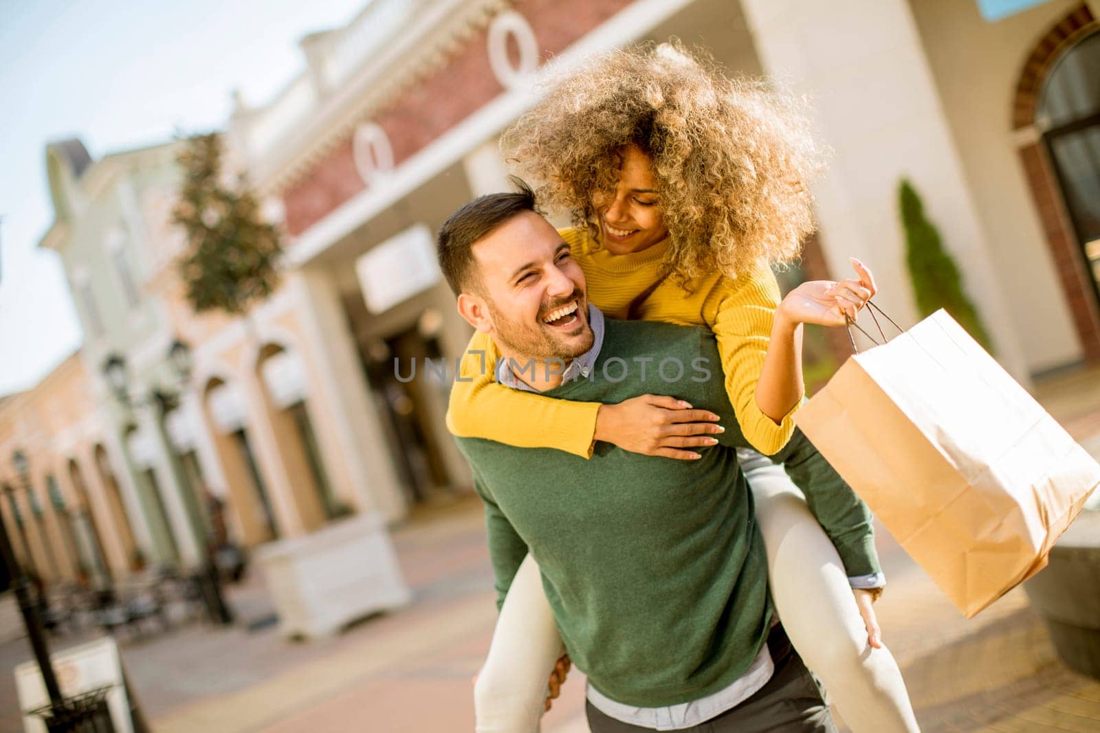 Portrait of  young man holds young woman on his back , have fun and go to shopping