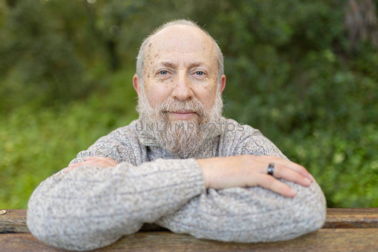 Smiling senior man enjoying retirement relaxing in park with folded arms on wooden bench