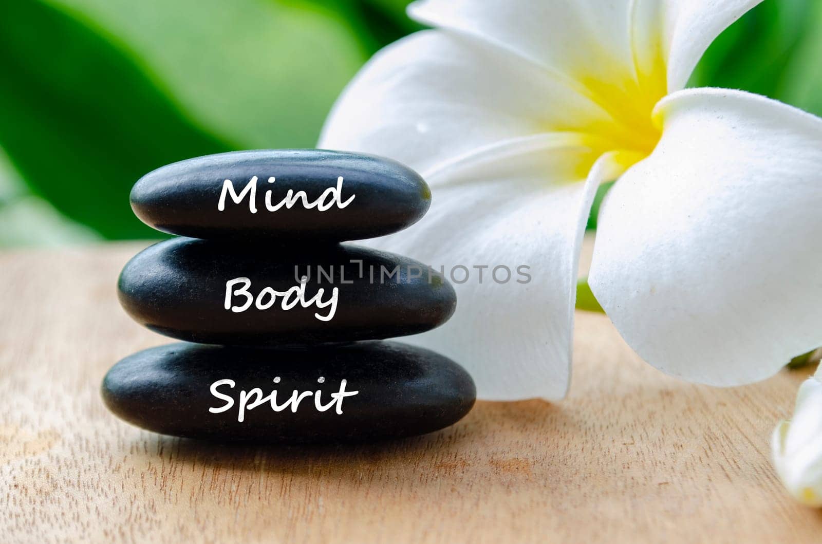 Mind, Body and Spirit text on black zen stones with beautiful white flower background.