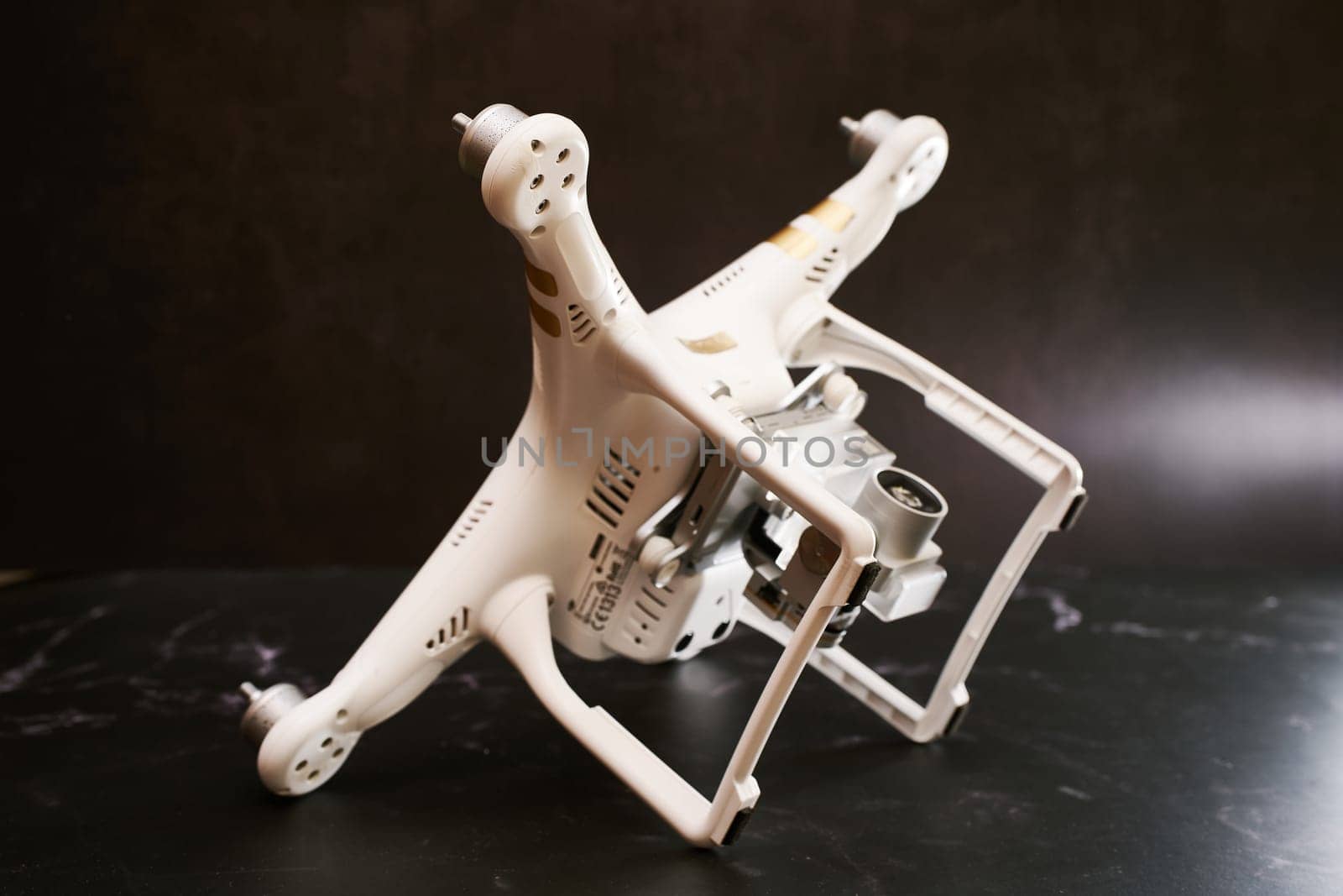 White drone without propellers DJI Phantom 3 lies on its side on stands on a black table. High quality photo