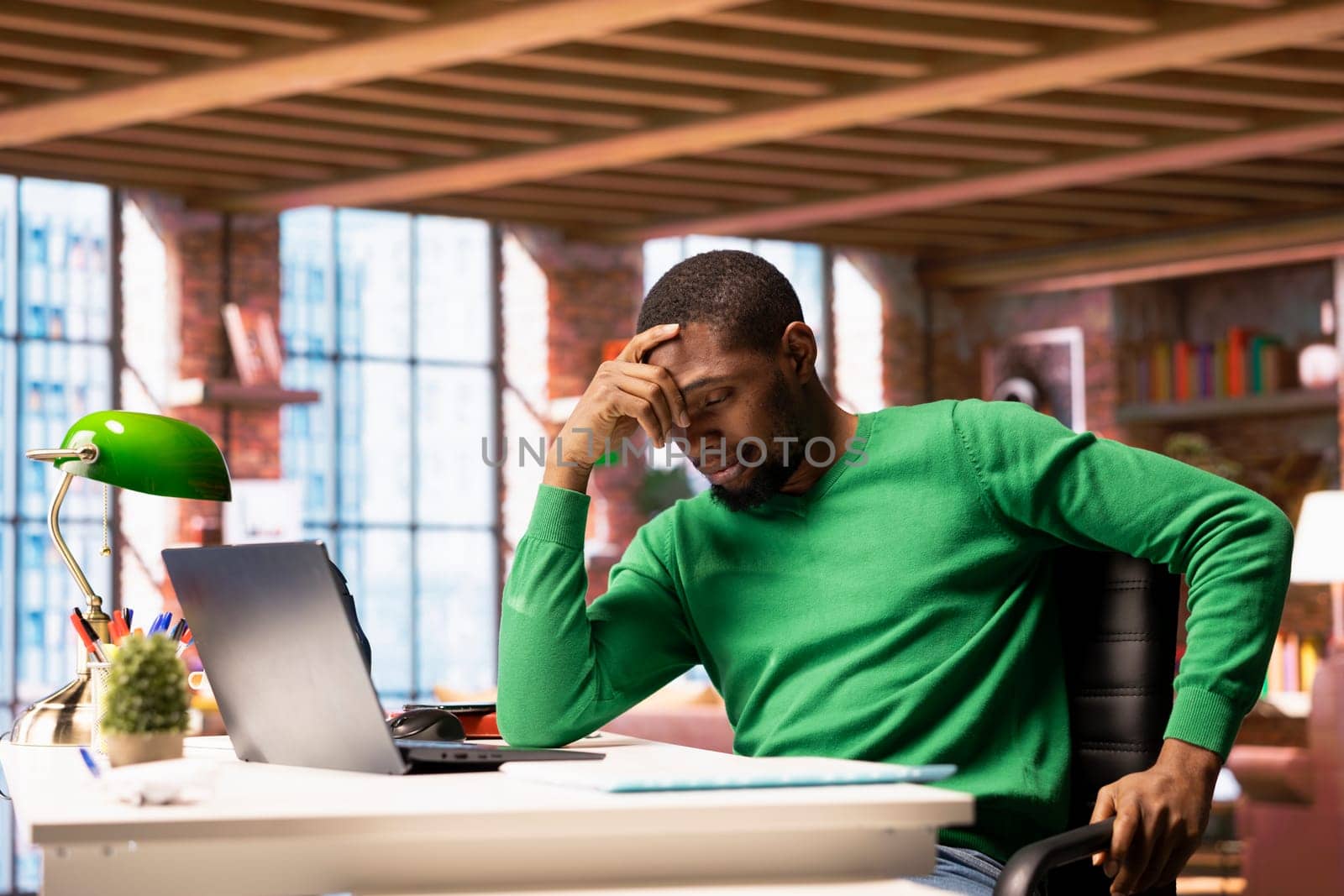 Remote employee at home office desk waiting for laptop operating system to open, feeling bored. Impatient african american man frustrated by long wait time while using software on notebook