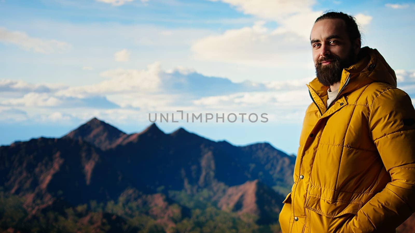 Hiker dressed in warm clothing stands on a mountain peak after climbing to the top, gazing at the breathtaking landscape of rugged hills and vast sky. Adventure with scenic view. Camera A.