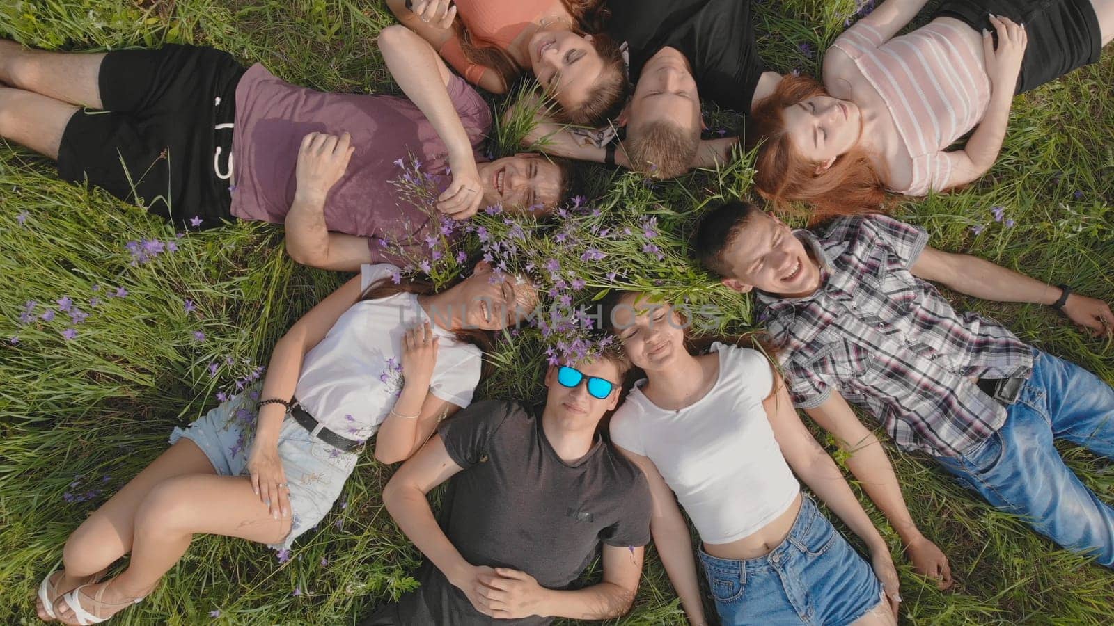 Friends lie on the grass in the form of a figure of the sun. A drone rises and swirls above them