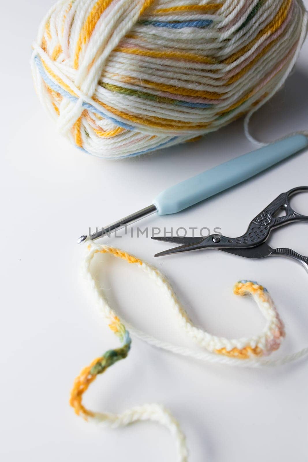 Colorful yarn ball with crochet hook and scissors on white background.