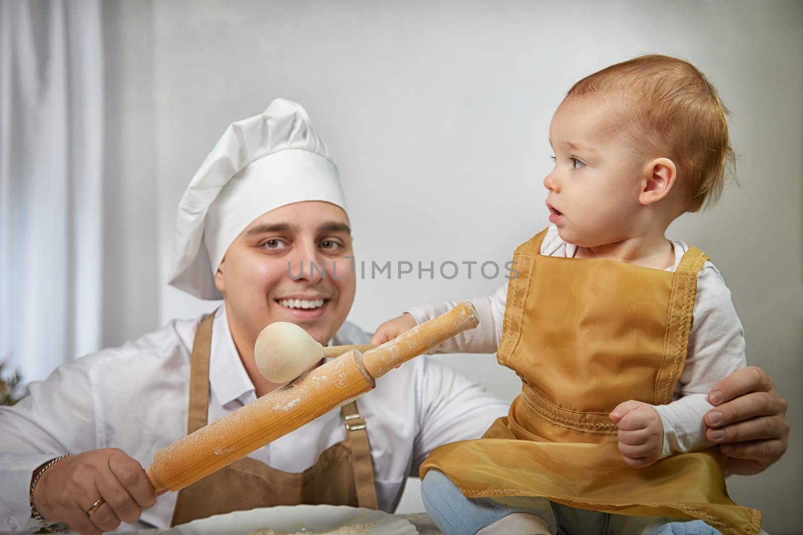 A family enjoys a fun cooking session, playfully covered in flour while engaging with their little ones in a warm kitchen. Father and son having fun