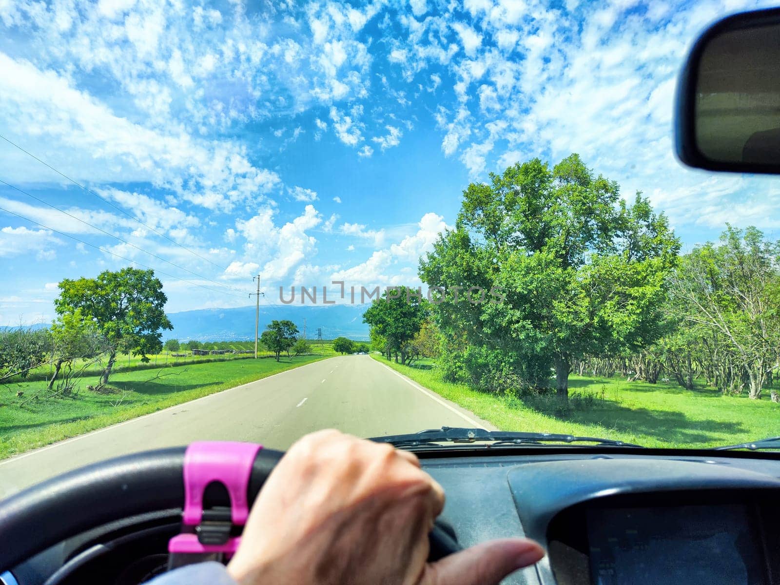 Traveling along a winding road, a hand on the steering wheel, with vibrant green hills and a bright blue sky ahead.