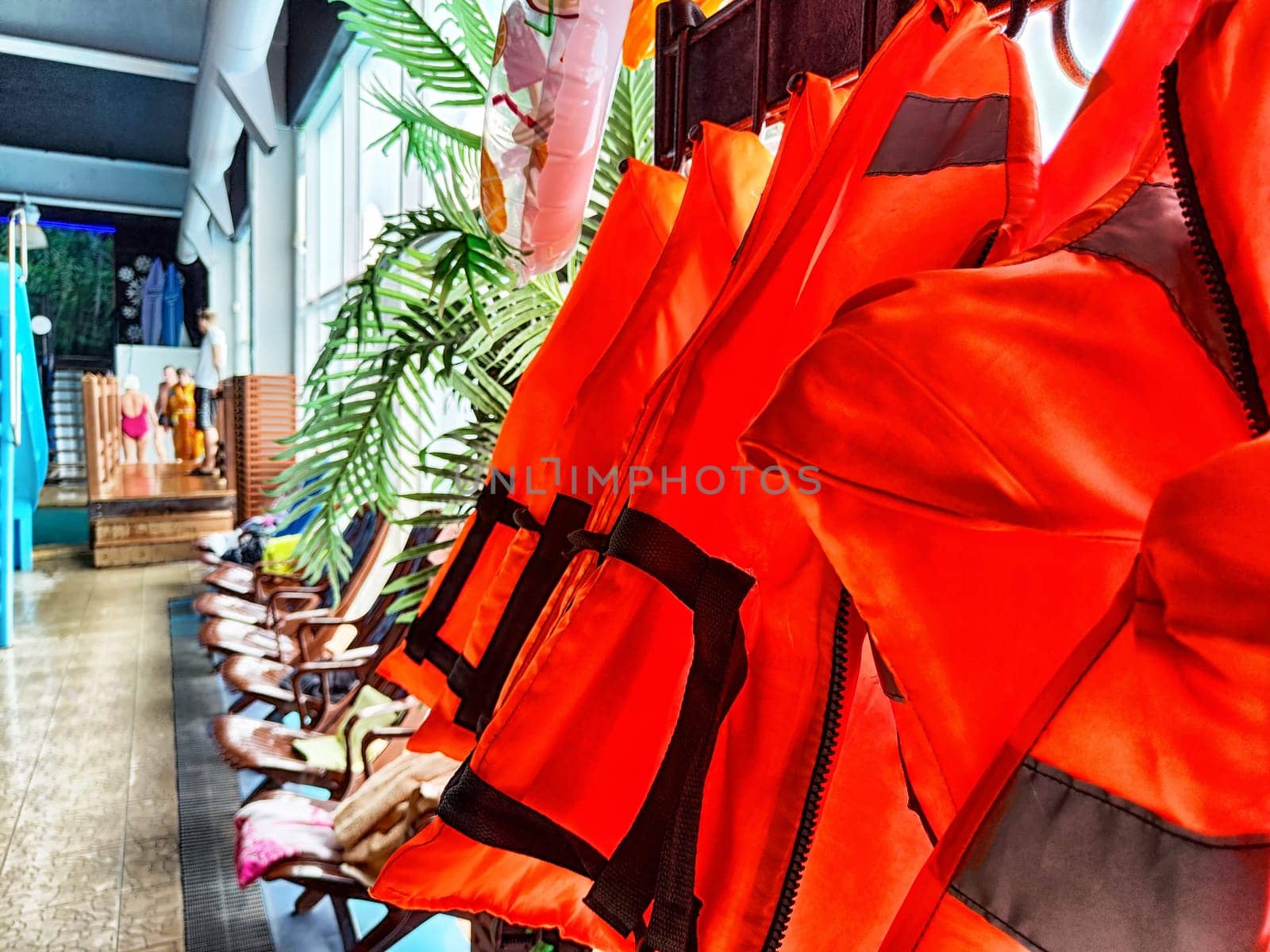 Bright orange life jackets are lined up beside a tropical-themed pool area, prepared for use during water activities and swimming lessons.