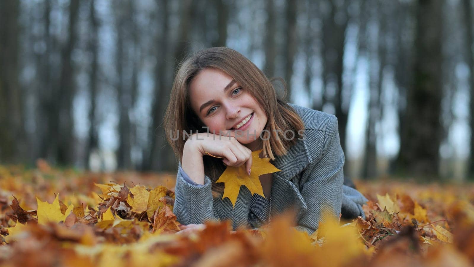 Beautiful happy young girl with a smile holds an autumn yellow leaf near the face