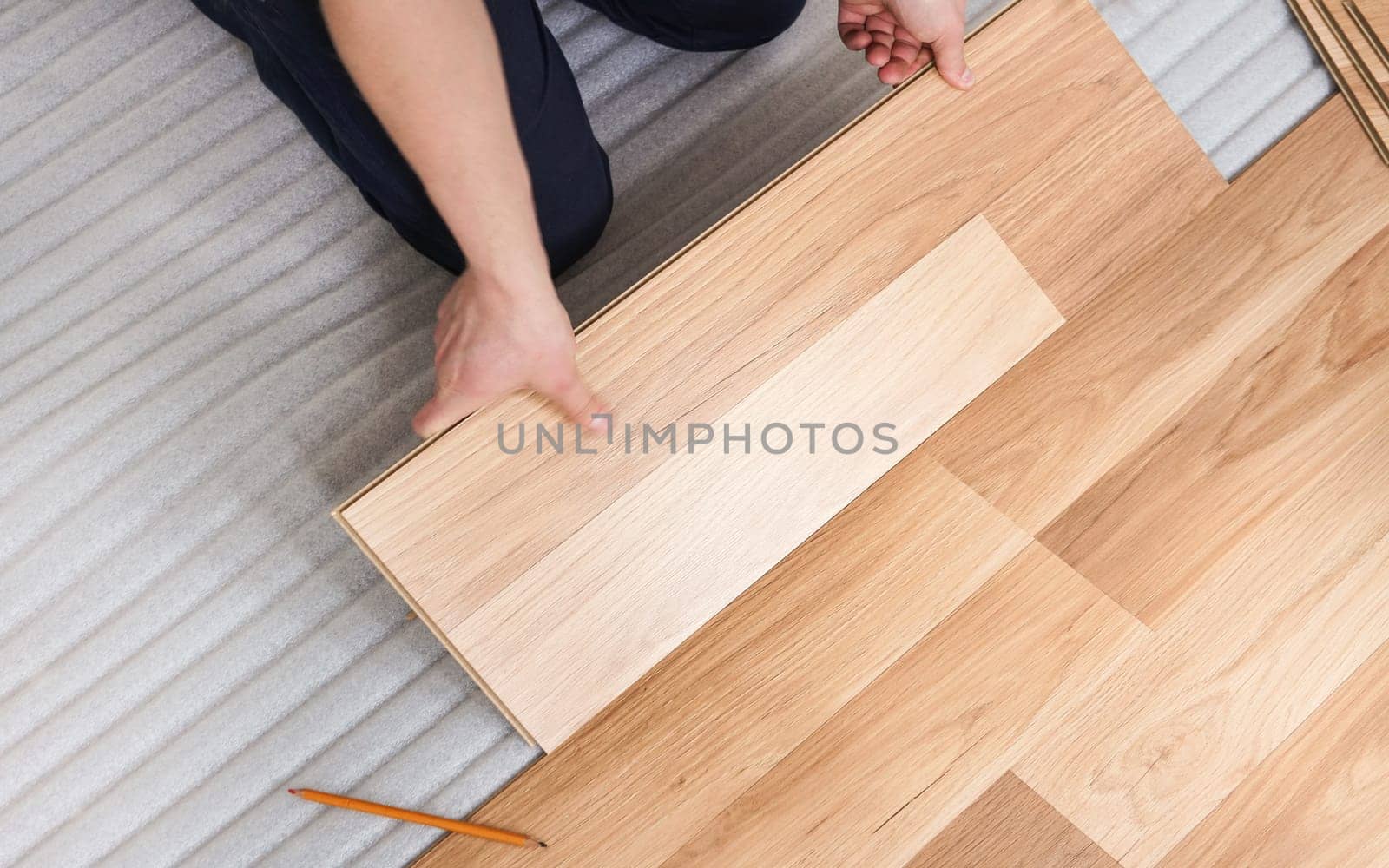 Installing laminated floor, detail view from above on man hands holding wooden tile, fitting it, over white foam base layer