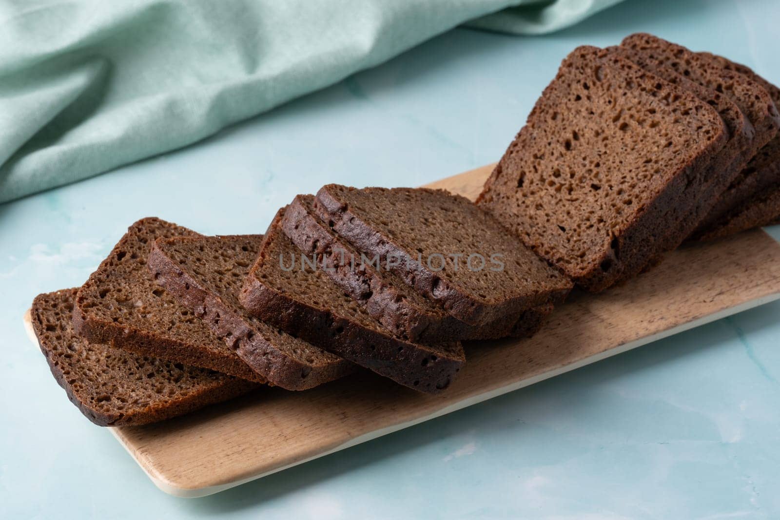 Slices of dark rye bread arranged neatly on a wooden platter against a soft green background.