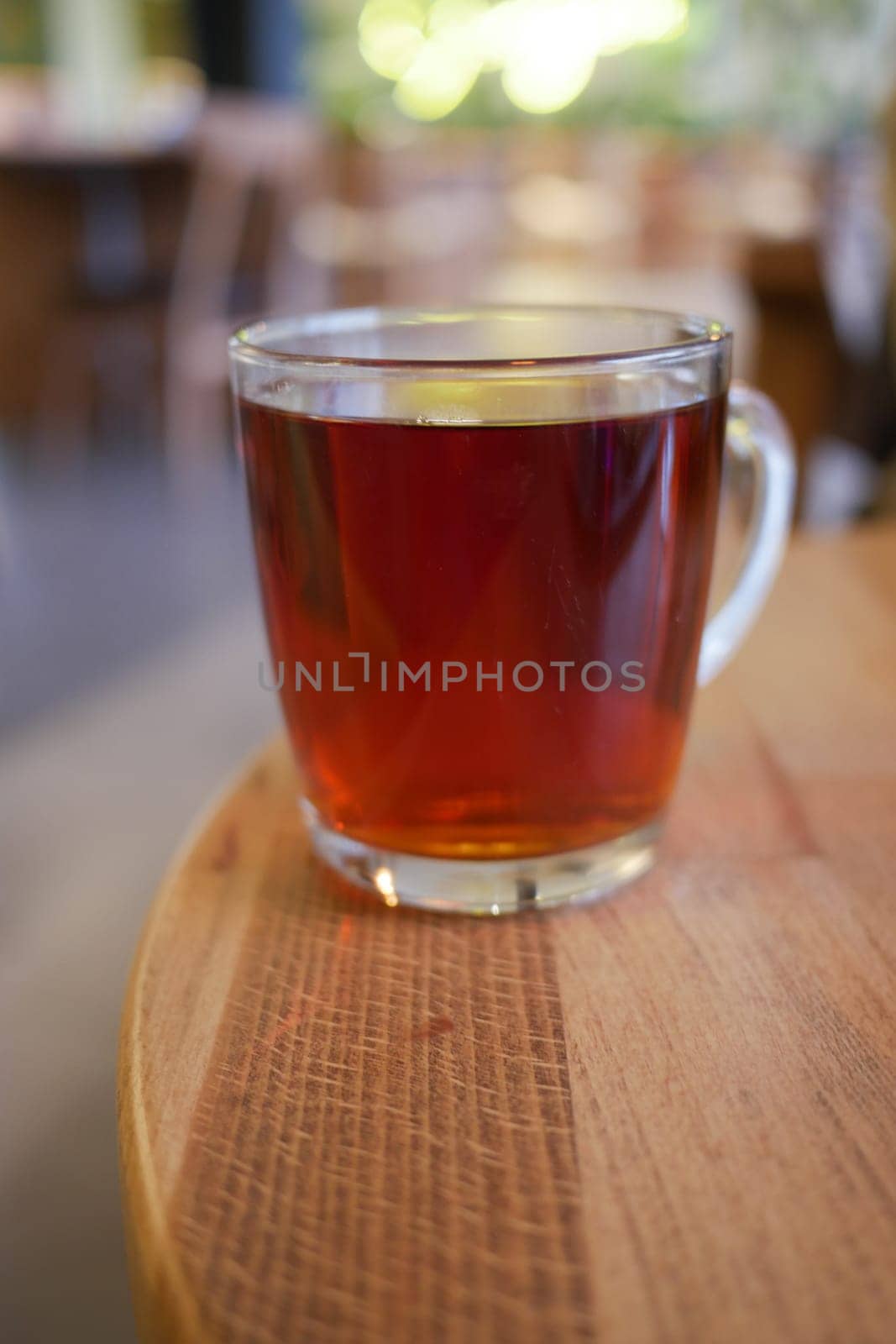 A clear cup filled with dark herbal tea rests on a wooden table.