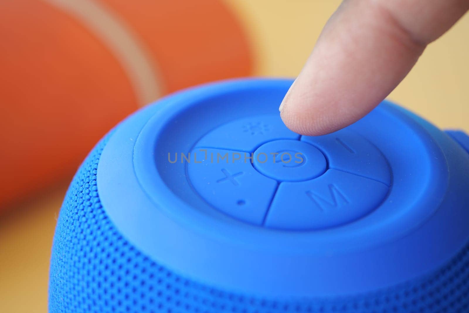 A finger is pressing a button on a blue portable speaker during use.