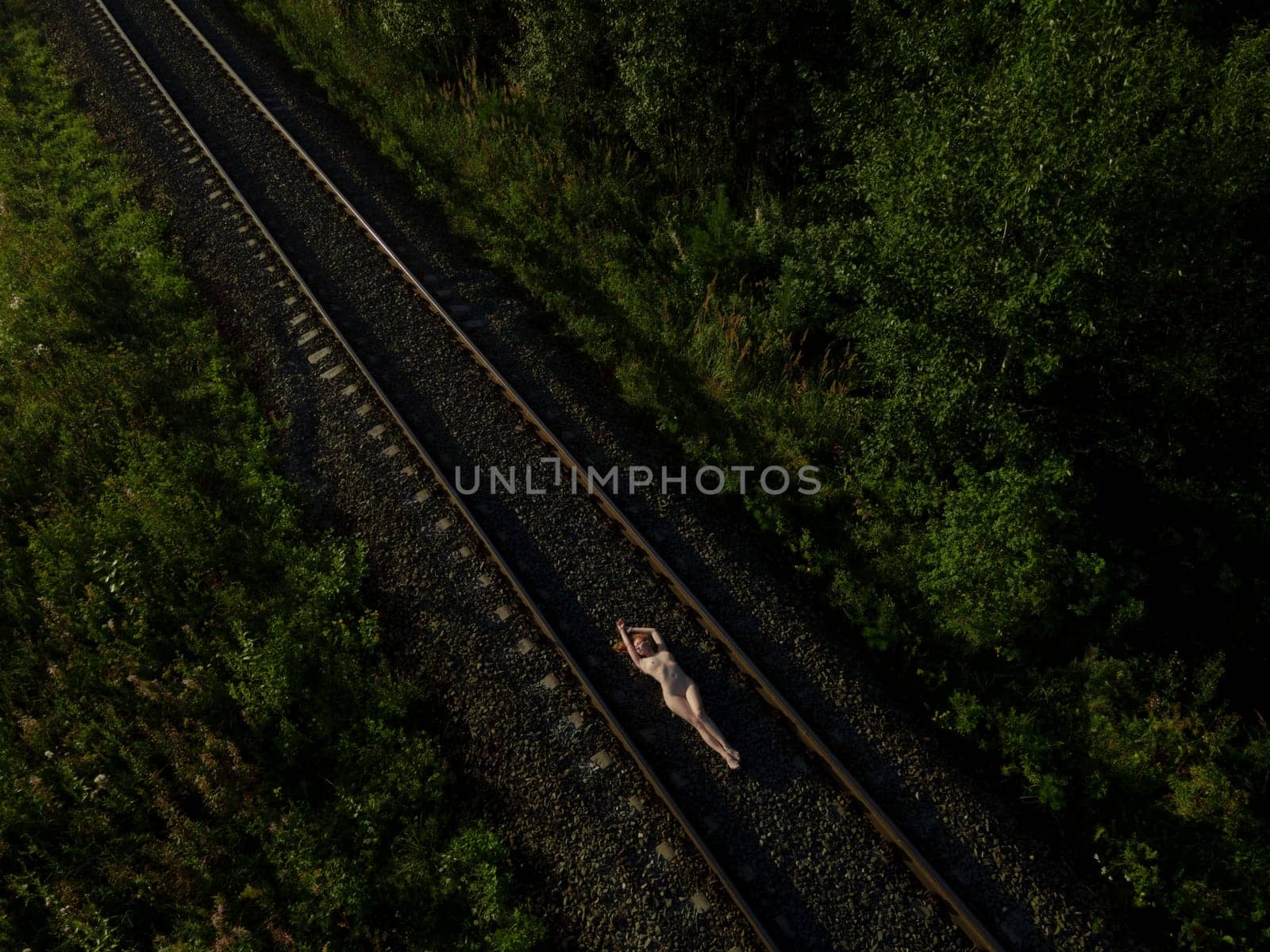 Top view of naked female in lying on rail road at sunrise