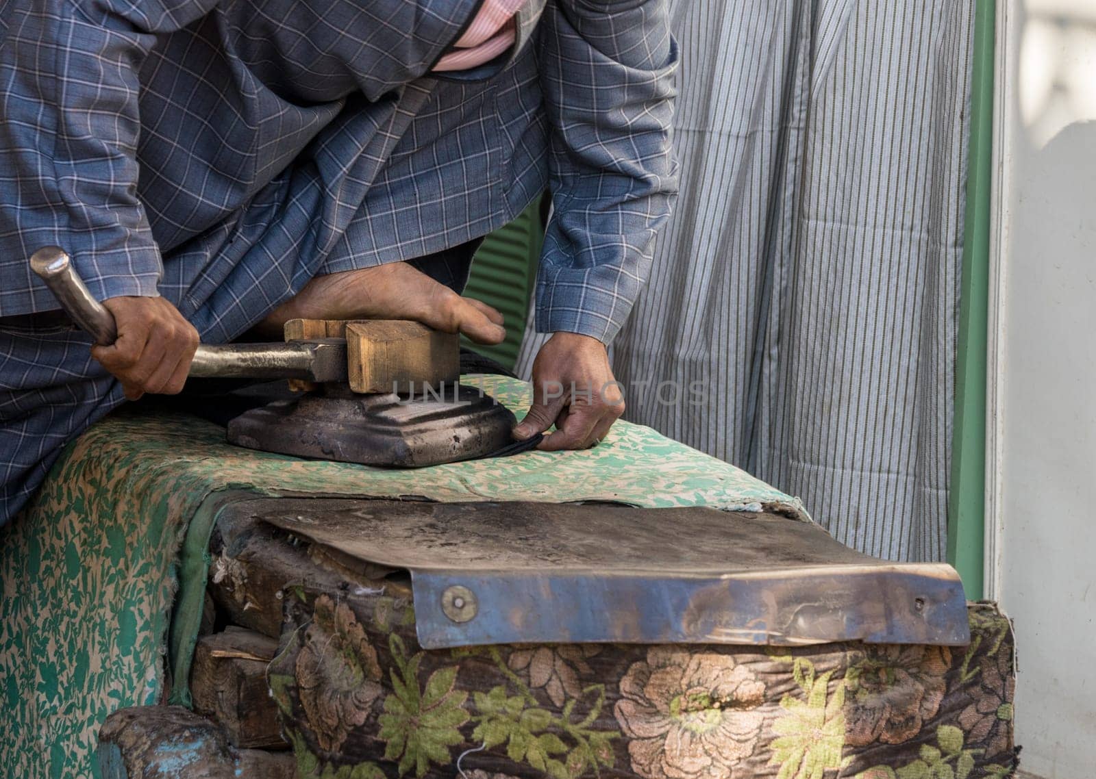 A tailor skillfully uses a foot-operated iron to smooth material in Esna, Egypt, showcasing traditional tailoring techniques