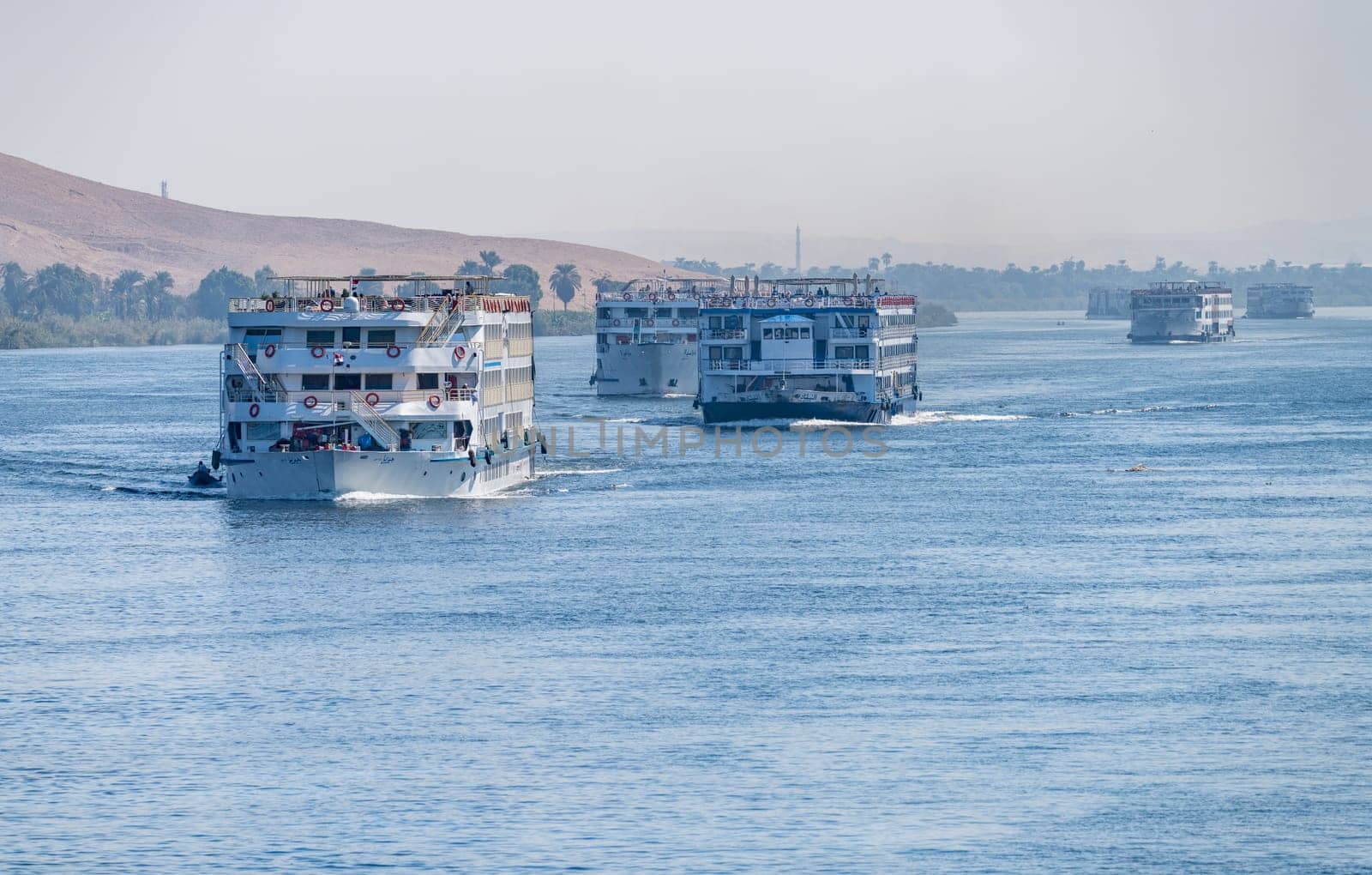 Esna, Egypt - 3 November 2024: Multiple river cruise ships make their way down the Nile towards Esna with desert in background