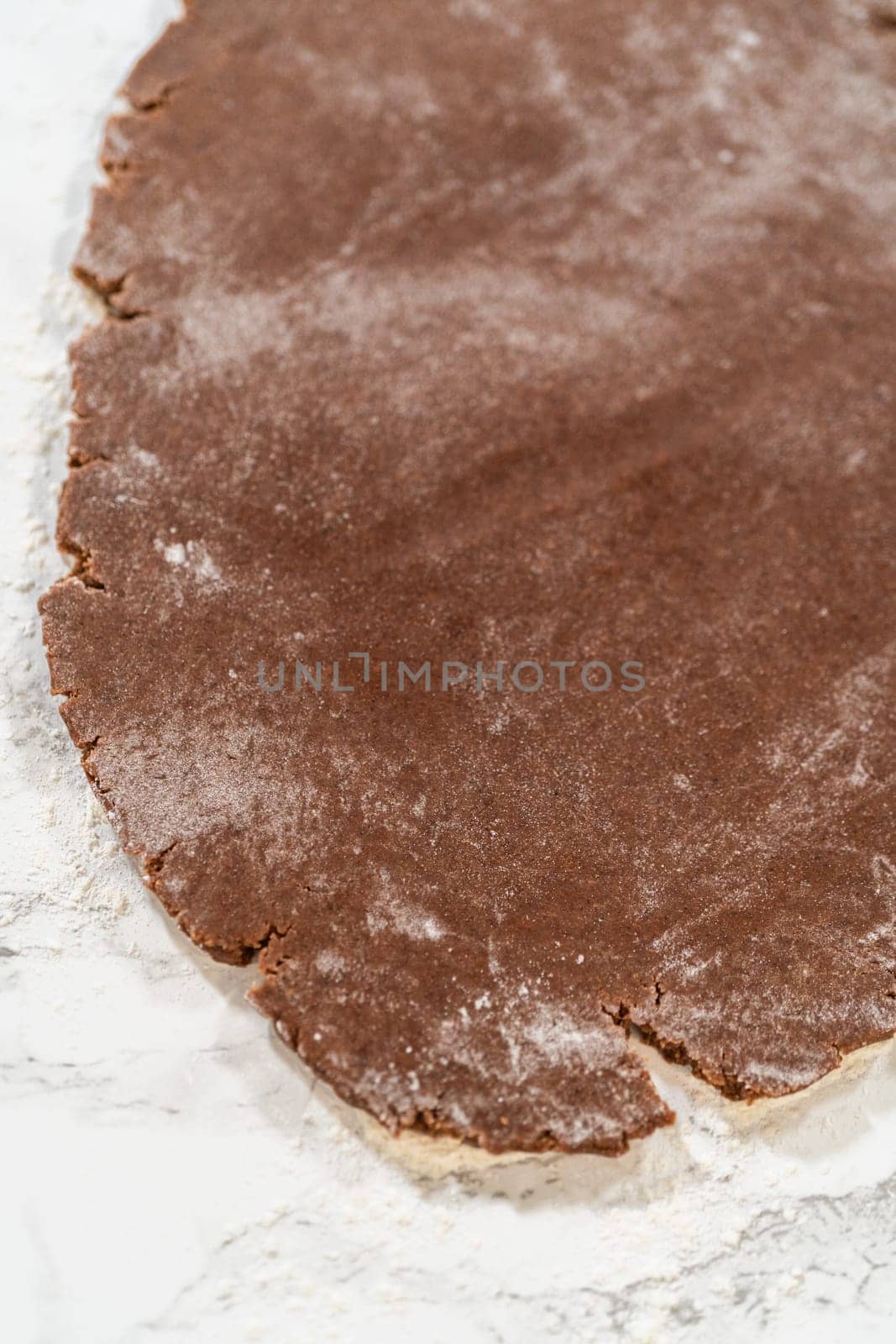 Overhead view of flattened dough for Pale Gingerbread Cookies on a floured marble surface, prepared for cutting out mitten shapes.
