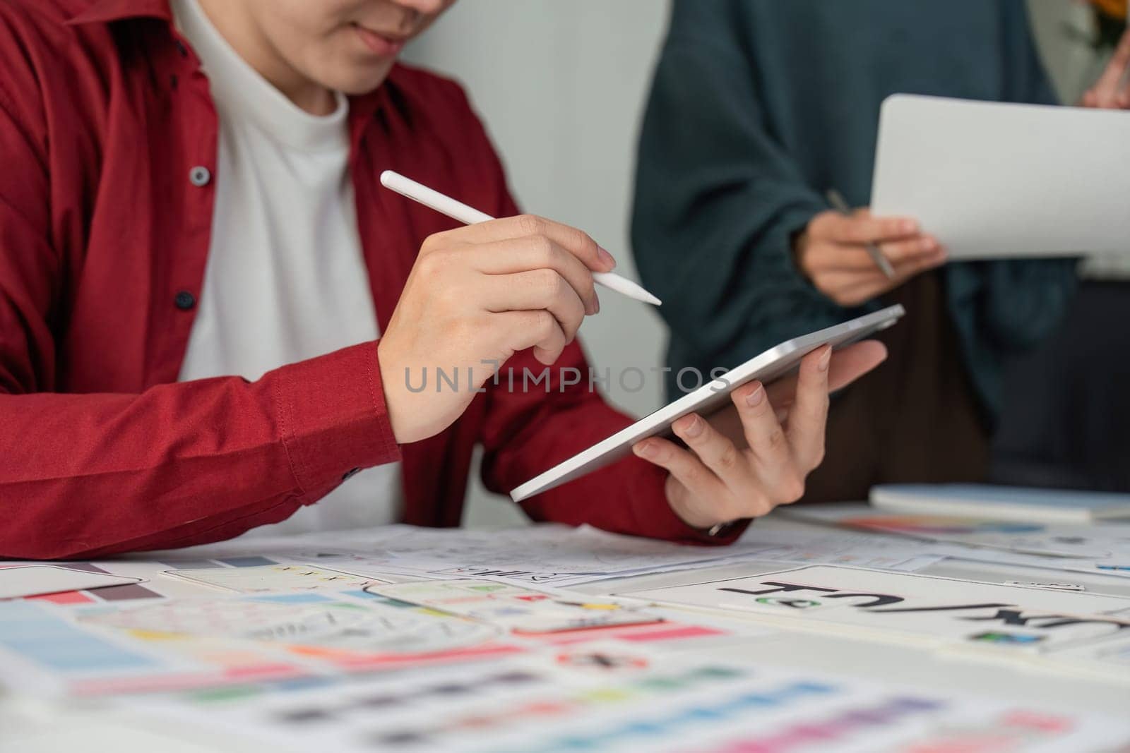 A designer is focused on a digital interface with a tablet in hand, working alongside her team on refining UIUX elements.