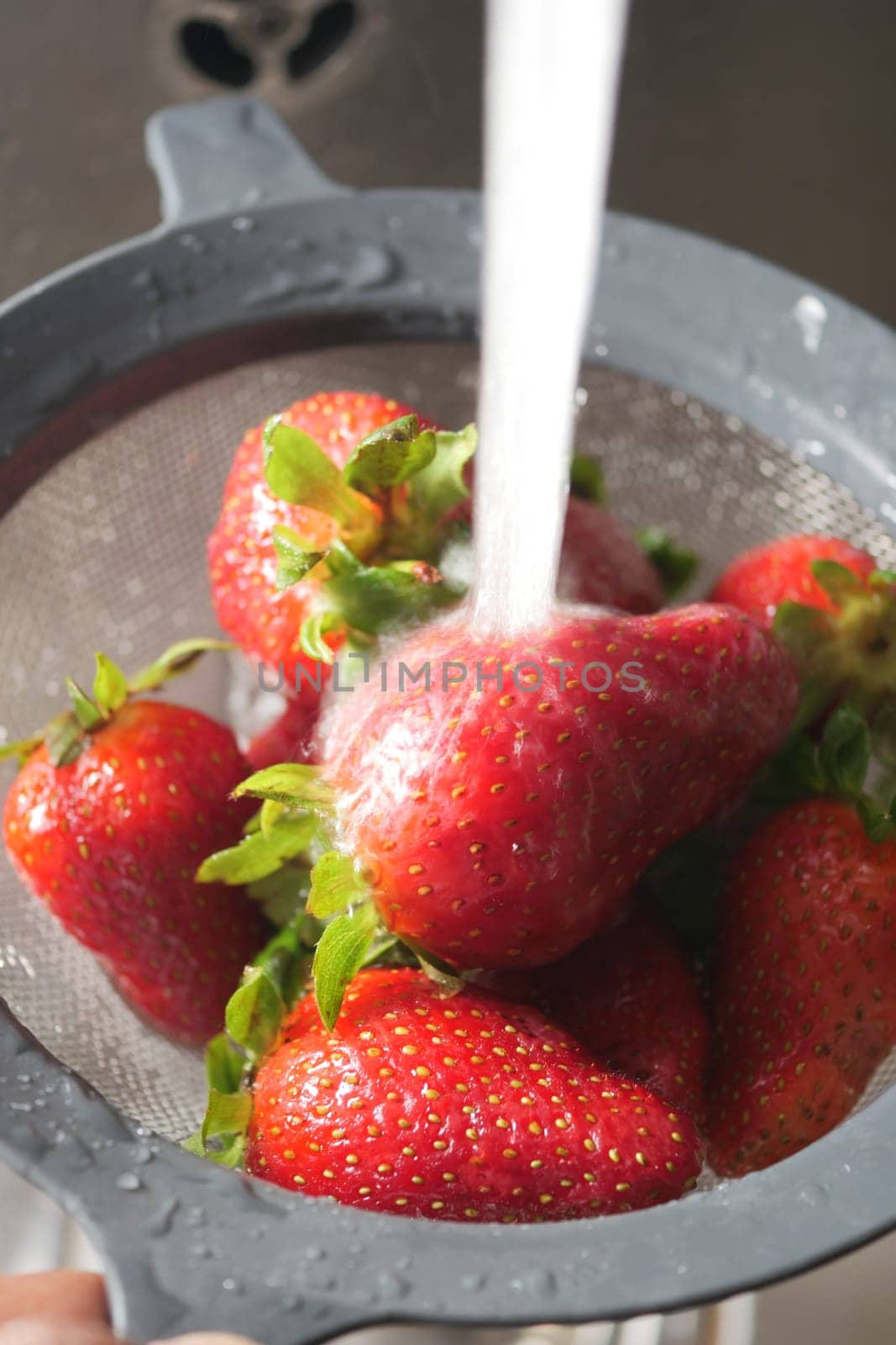 Juicy strawberries are cleaned in a colander as water cascades down.