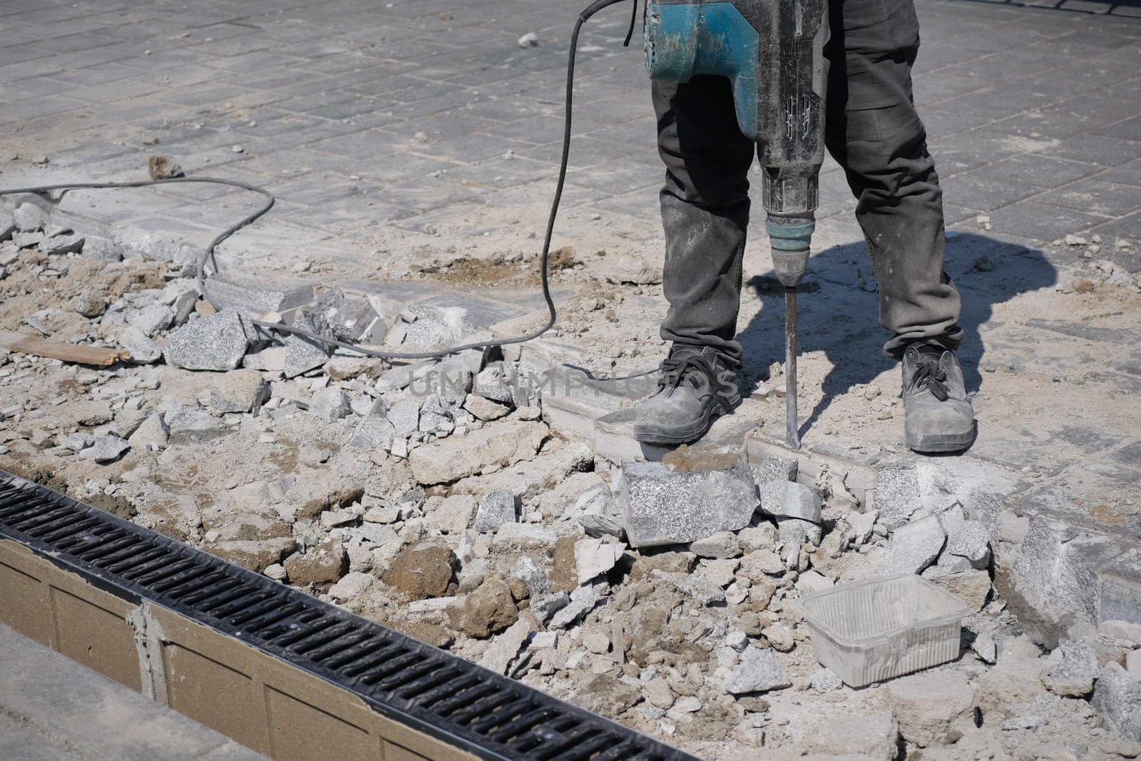A construction worker operates a jackhammer on broken pavement during a project.
