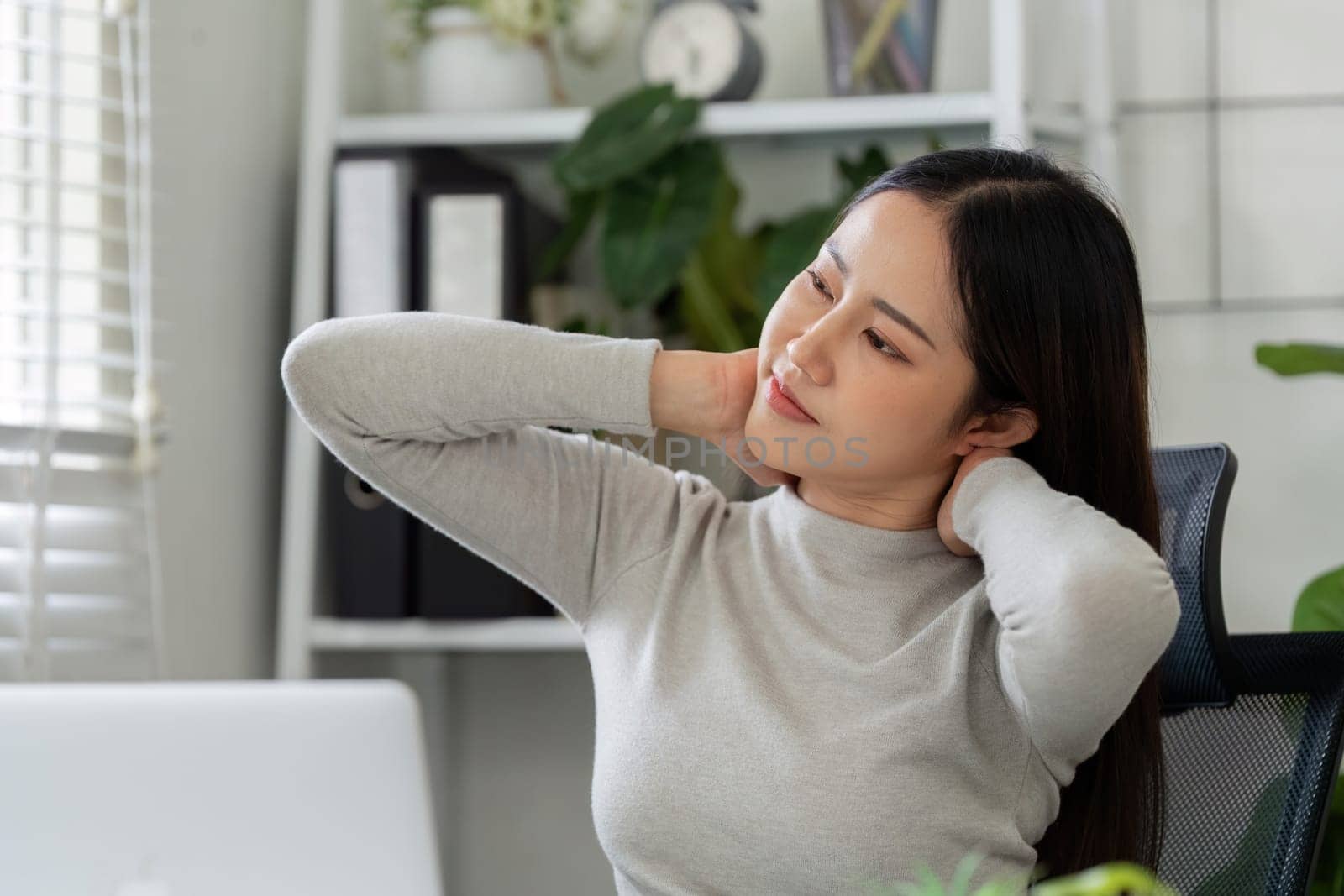 Taking a moment to stretch, the woman addresses her neck discomfort during a work session, balancing productivity with well-being in her home environment.