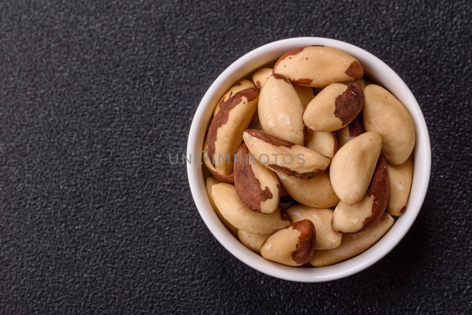 Brazil nut kernels in ceramic bowl on dark concrete background