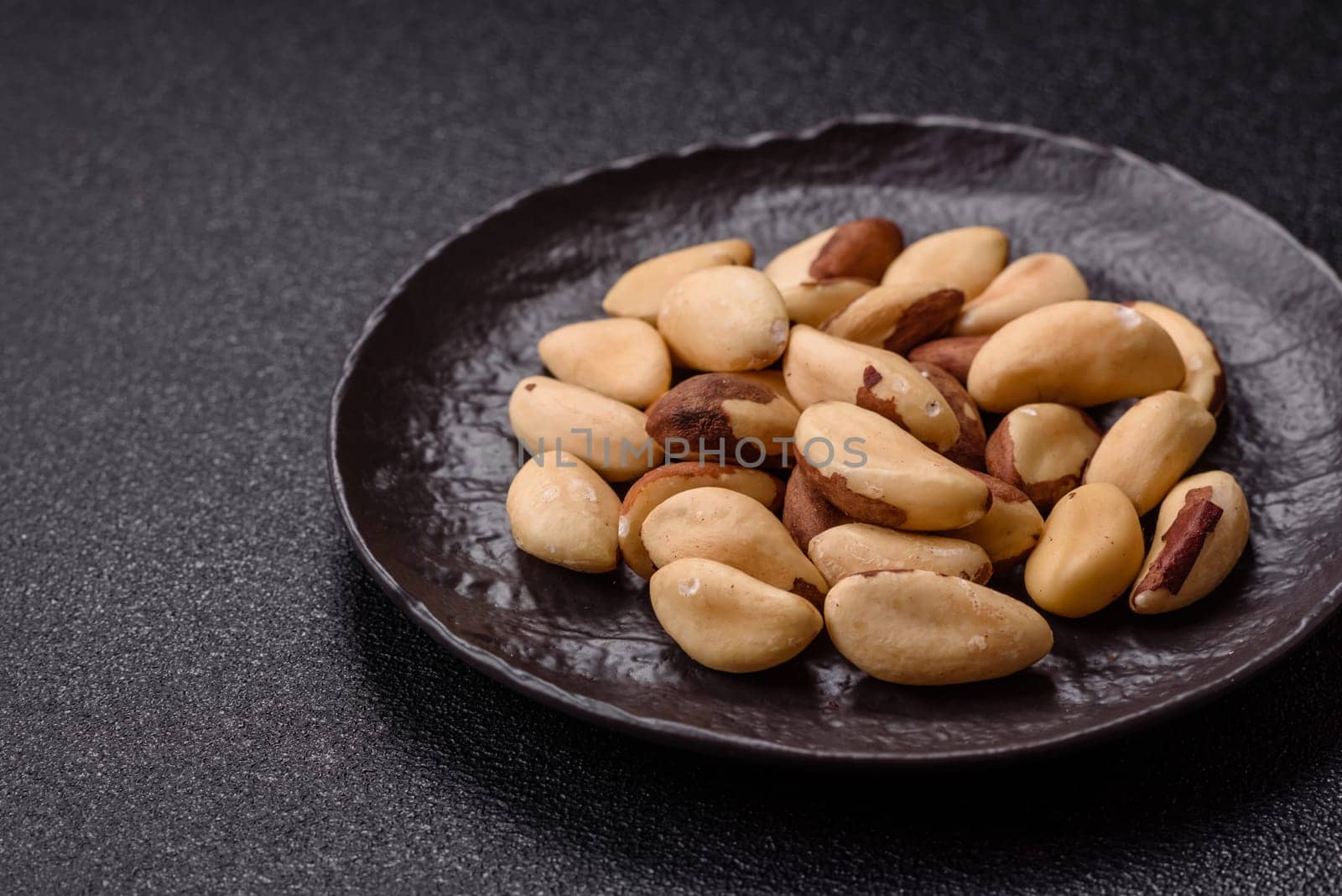 Brazil nut kernels in ceramic bowl on dark concrete background