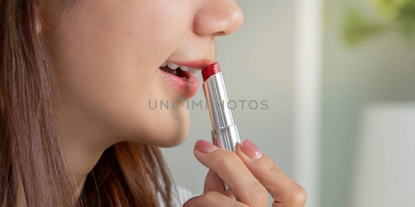 With a precise motion, the woman glides red lipstick on her lips, completing her glamorous look with confidence.
