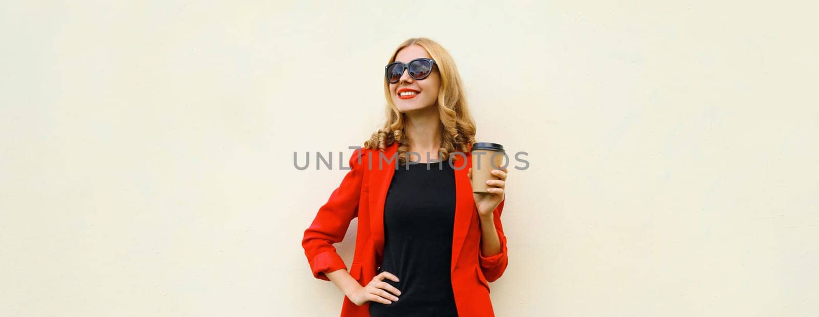 Stylish happy young woman in business suit, red blazer jacket with cup of coffee looking away standing on white studio background