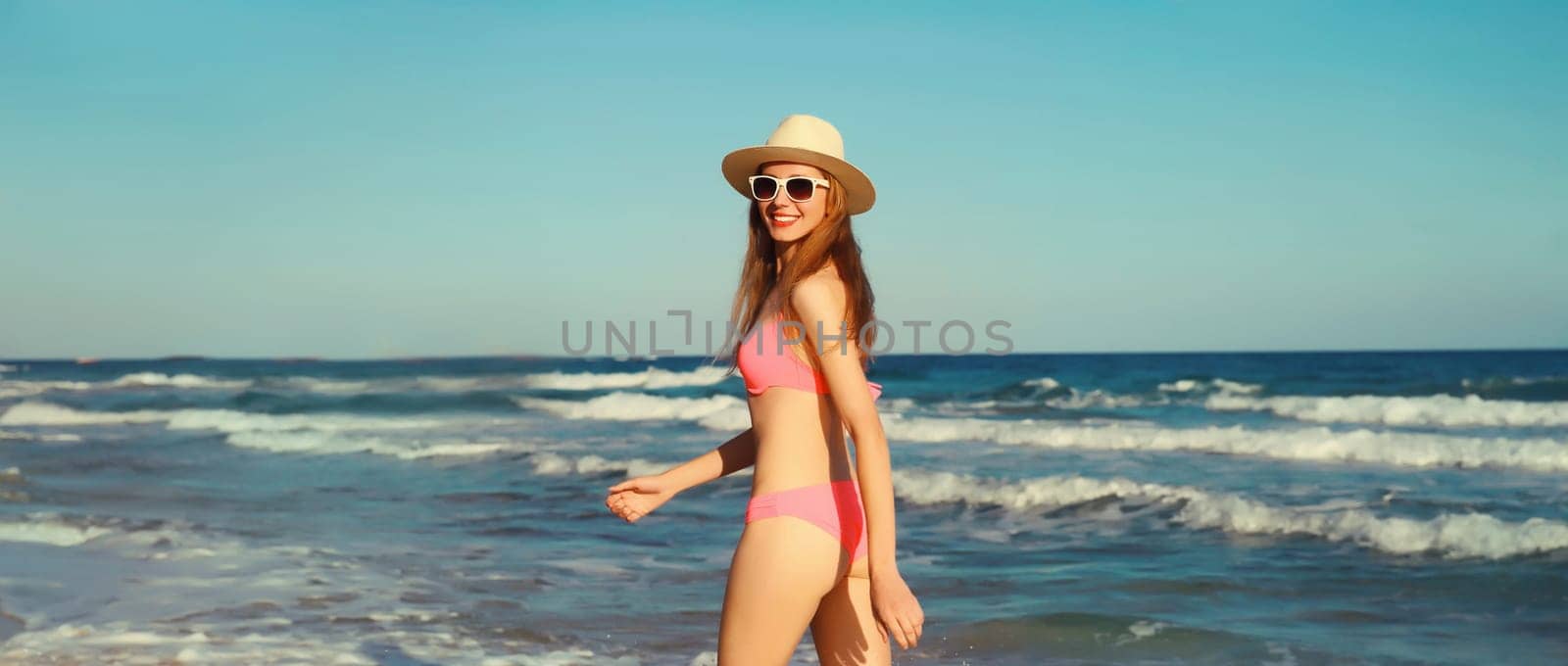 Summer vacation, happy joyful woman walking running in bikini swimsuit and tourist straw hat on the beach on sea coast with waves background on sunny day