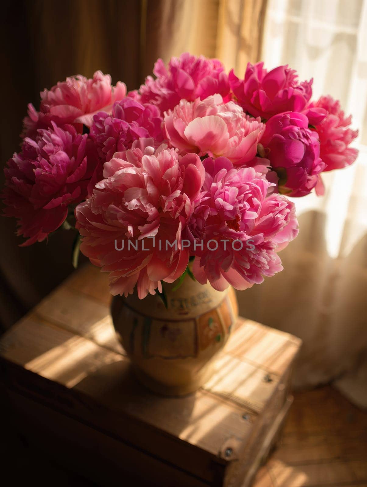 A vibrant bouquet of pink peonies fills a decorative vase, positioned on a wooden table. Sunlight streams through a nearby window, enhancing the colors and creating a warm atmosphere.