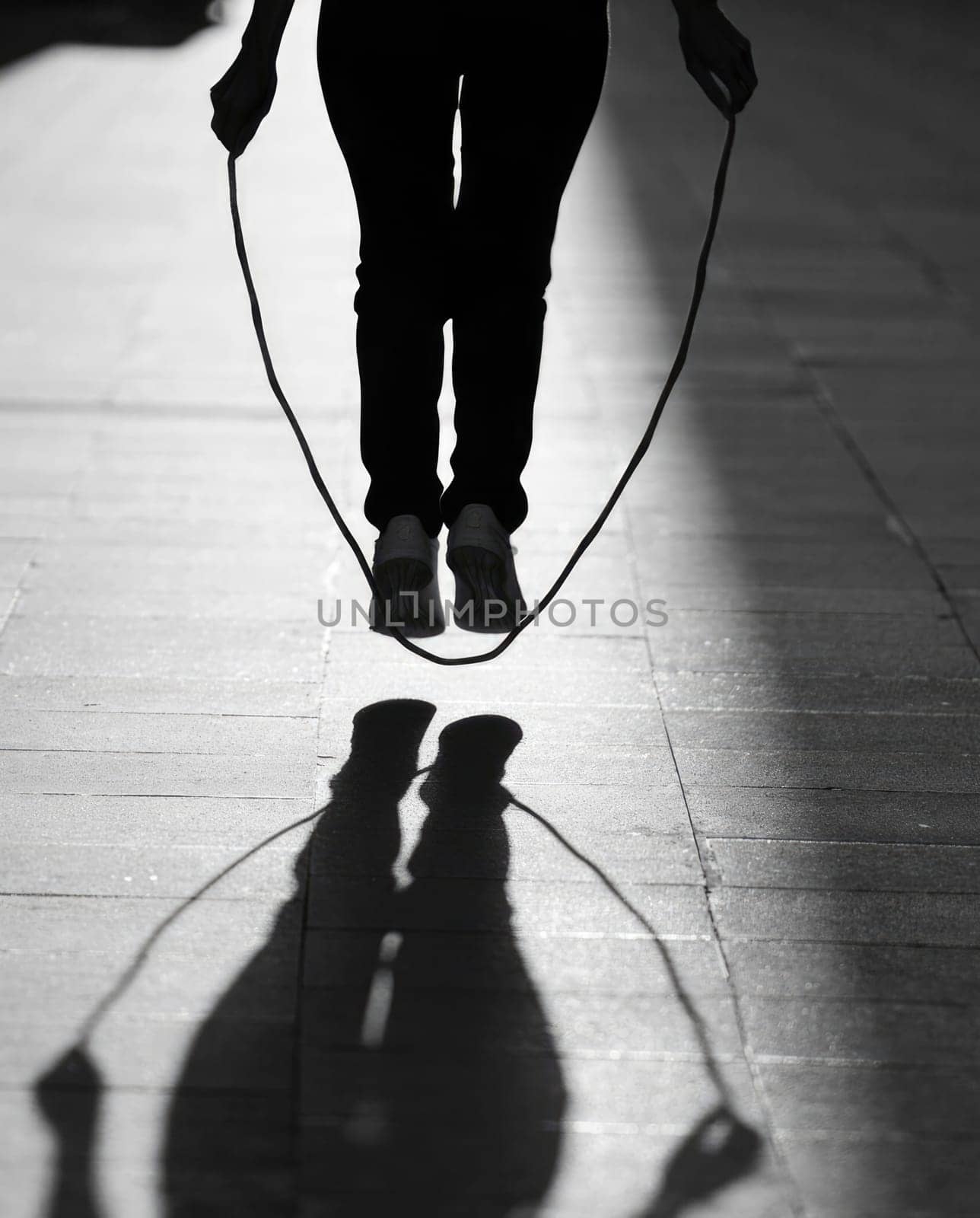 A person is captured in mid air while skipping rope, casting a long shadow on the ground. The warm glow of the late afternoon sun enhances the urban atmosphere, emphasizing their movement.
