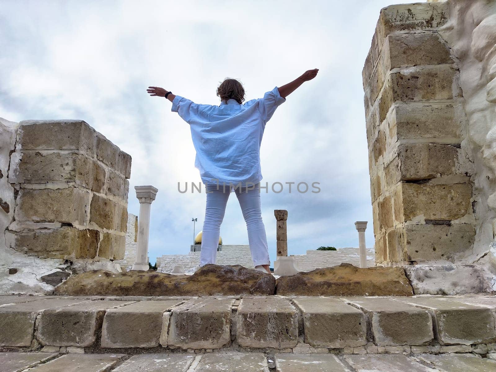 Tourist stands with arms wide open at ancient ruins, embracing the beauty of the location on her travel excursion.