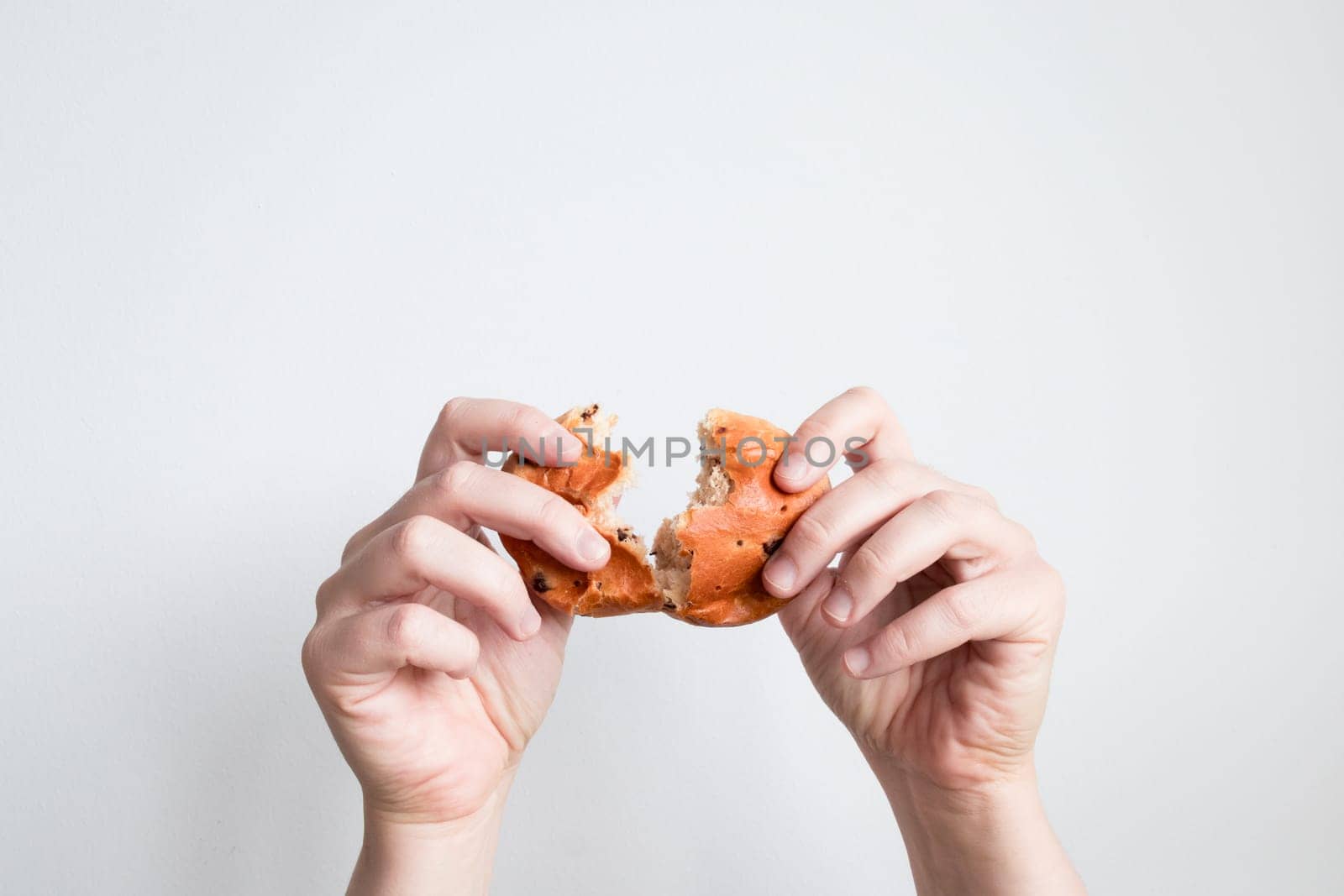 Hands breaking a bagel against a white background.