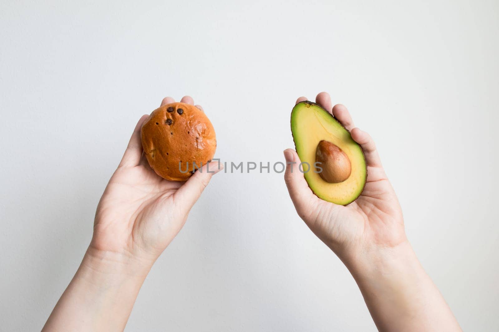 Hands holding avocado and cookie against white background.