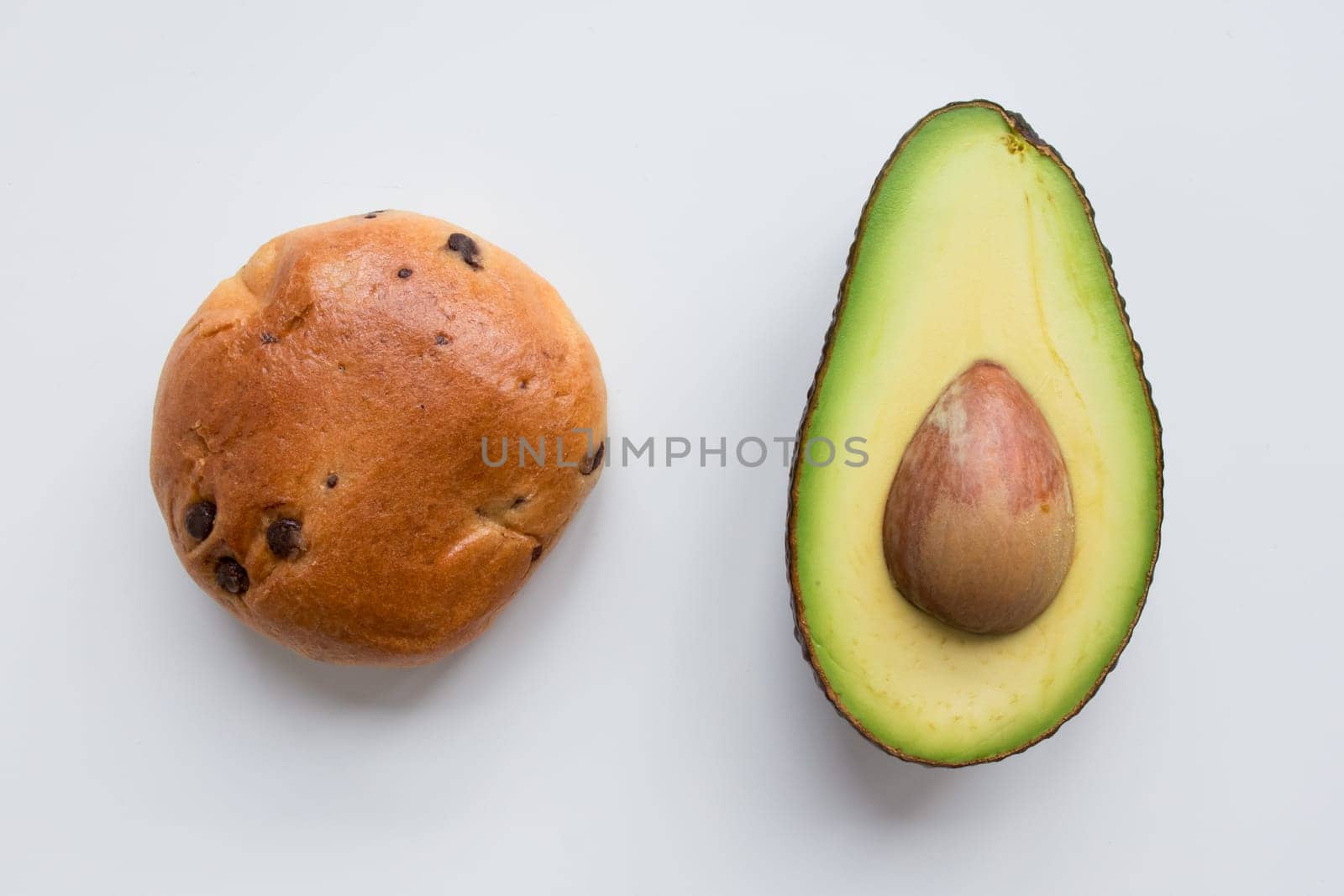 Chocolate chip bun and sliced avocado on white background.