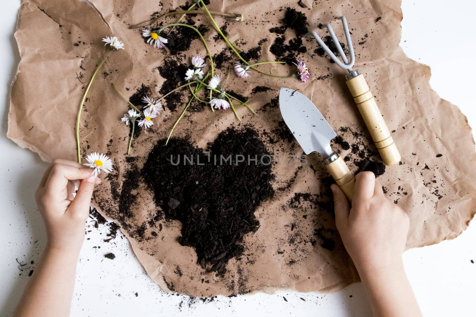 Gardening enthusiast tending floral heart arrangement on brown paper with tools.