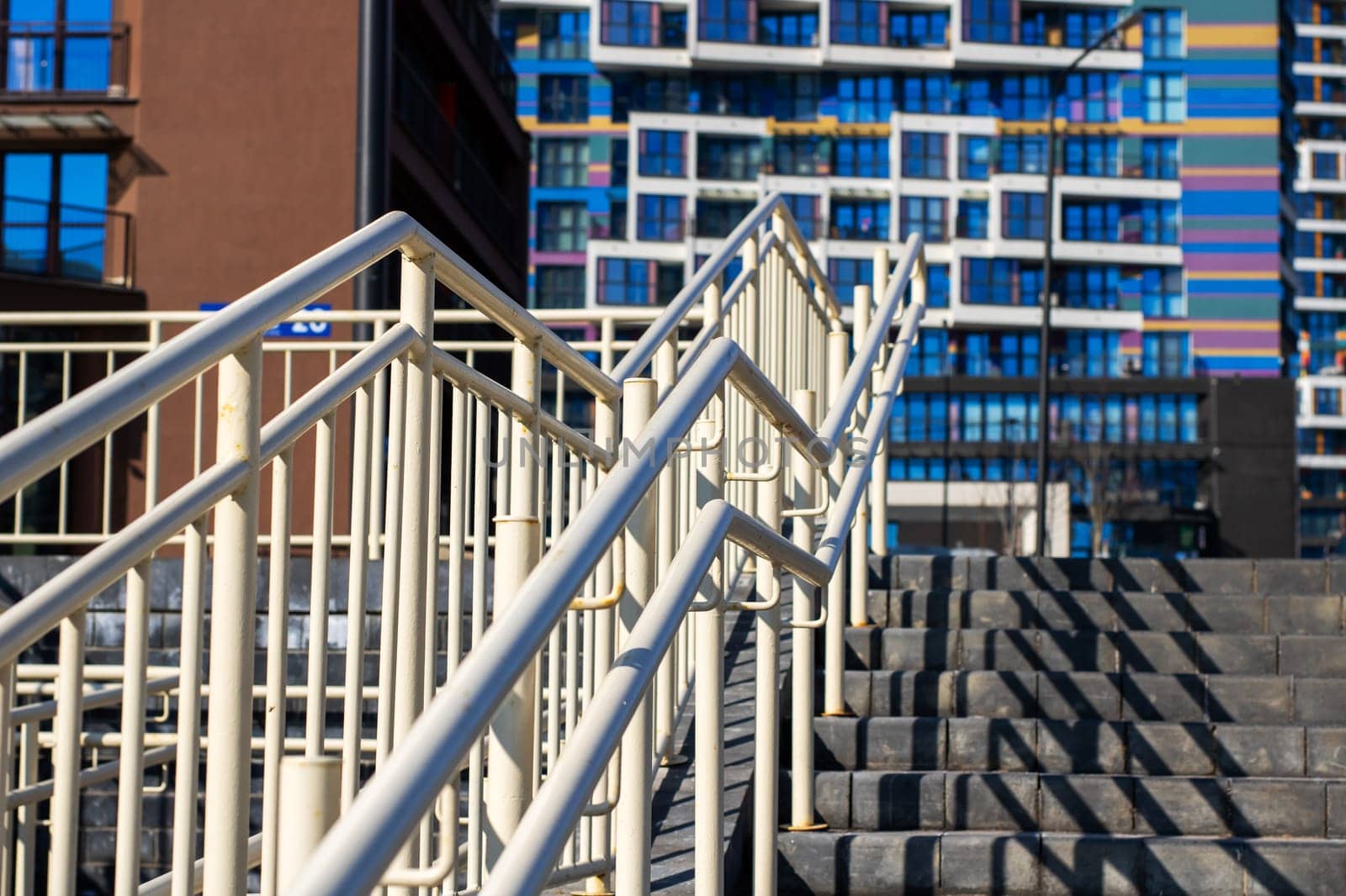A beautifully designed staircase with railings leads to modern buildings with colorful designs in the background