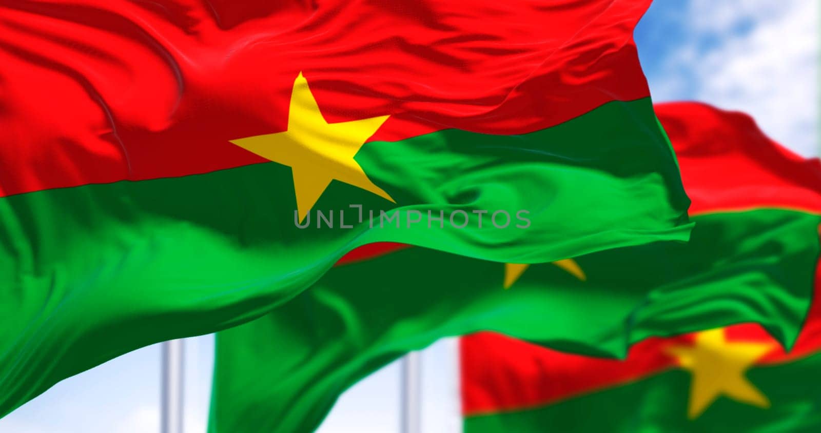 Multiple Burkina Faso flags waving in the wind with vibrant green, red and a yellow star. A symbol of unity, freedom, and progress. 3d illustration render. Rippled fabric.
