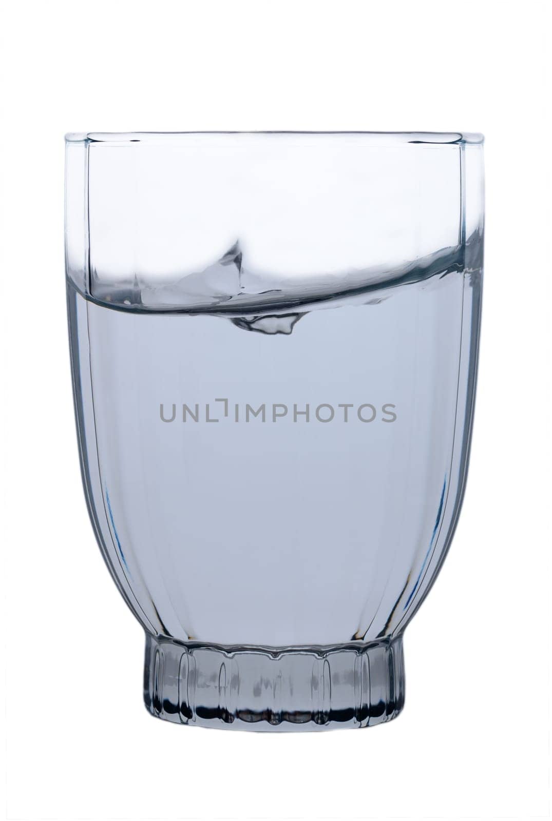 Droplets scatter as a splash disrupts the calm surface of translucent water in a uniquely shaped glass. Soft light accentuates the glass's contours, creating a moment of tranquil beauty.