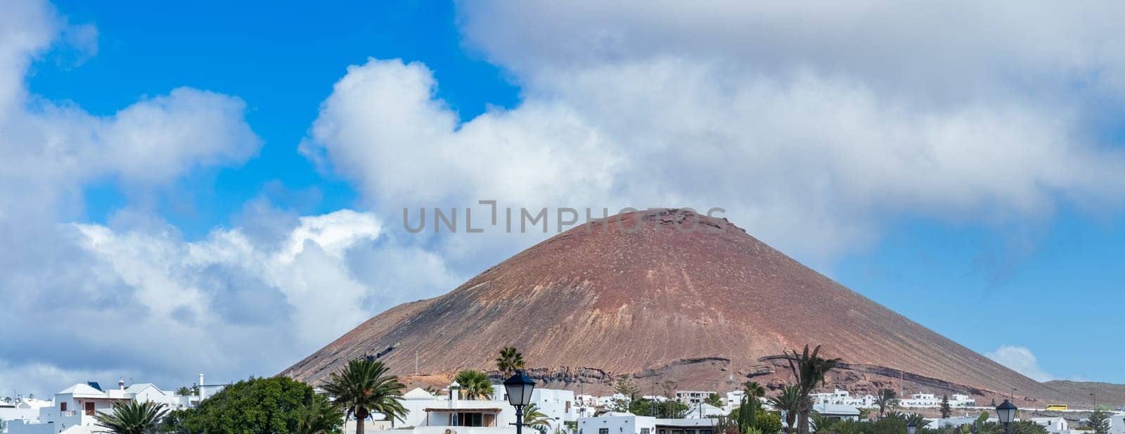 A stunning volcanic landscape in Lanzarote features white houses nestled beneath a majestic volcano under a vibrant blue sky.